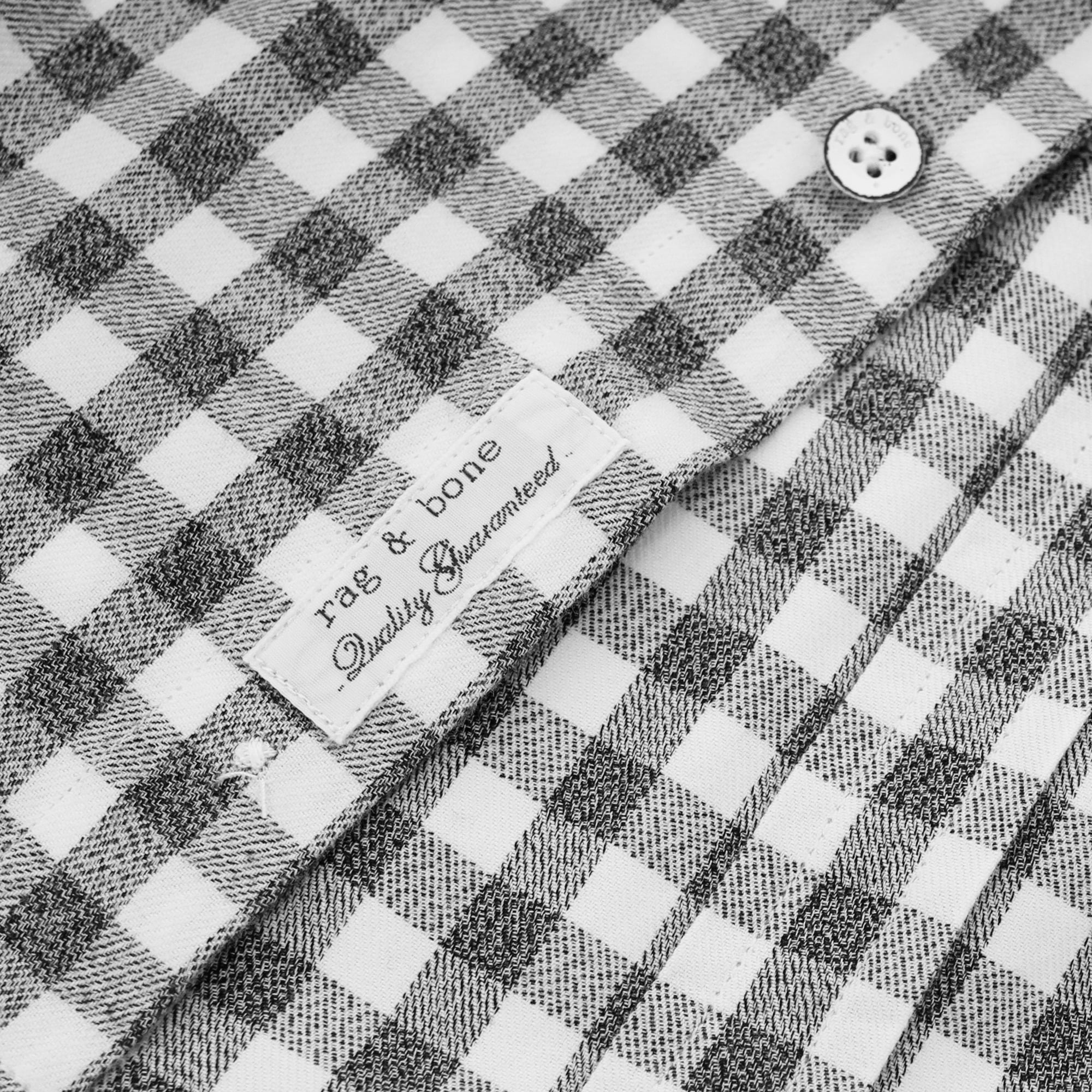 Close-up of the 'rag & bone Quality Guaranteed' label on a grey and white gingham shirt.