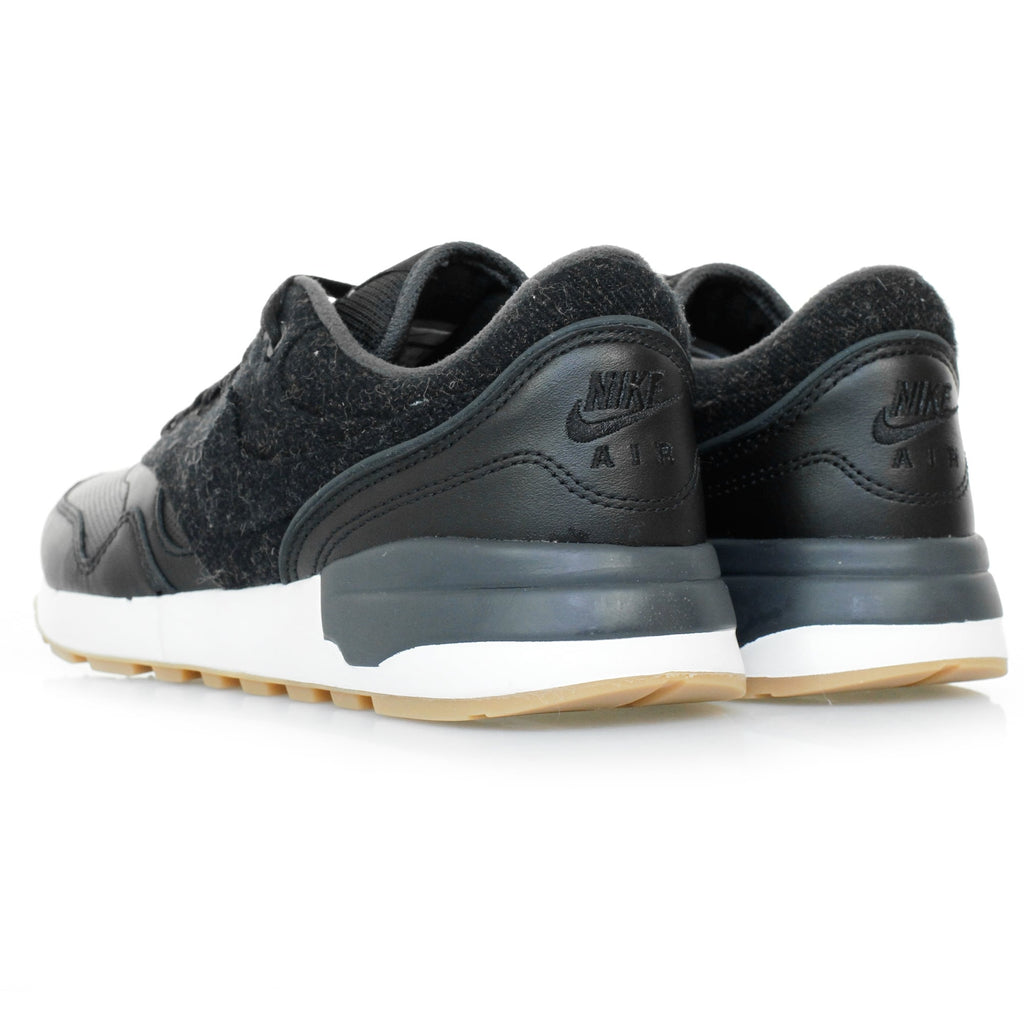 A pair of black trainers with textured uppers and white soles, viewed from the rear side.