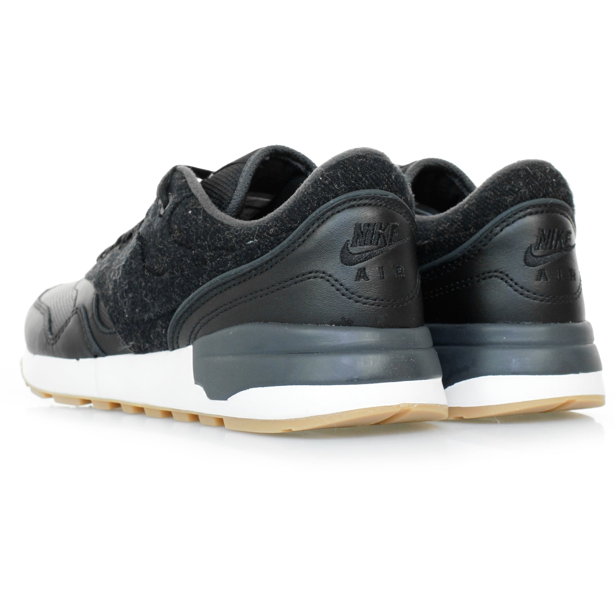 A pair of black trainers with textured uppers and white soles, viewed from the rear side.