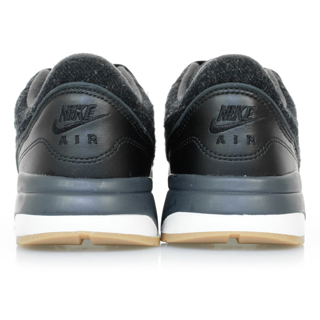 A pair of black trainers with textured uppers and white soles, viewed directly from the rear.