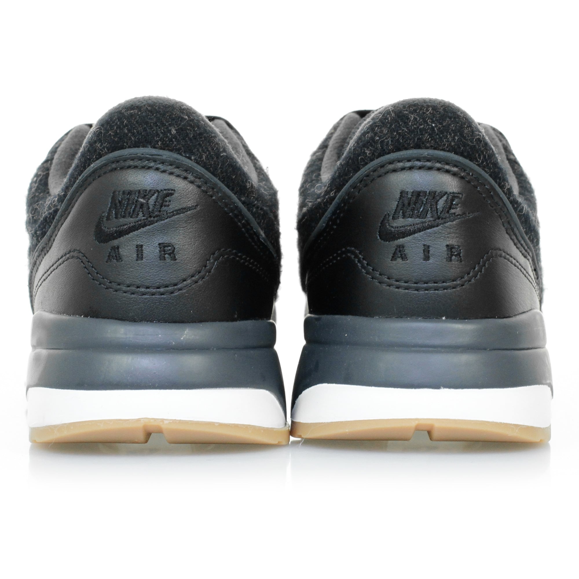 A pair of black trainers with textured uppers and white soles, viewed directly from the rear.
