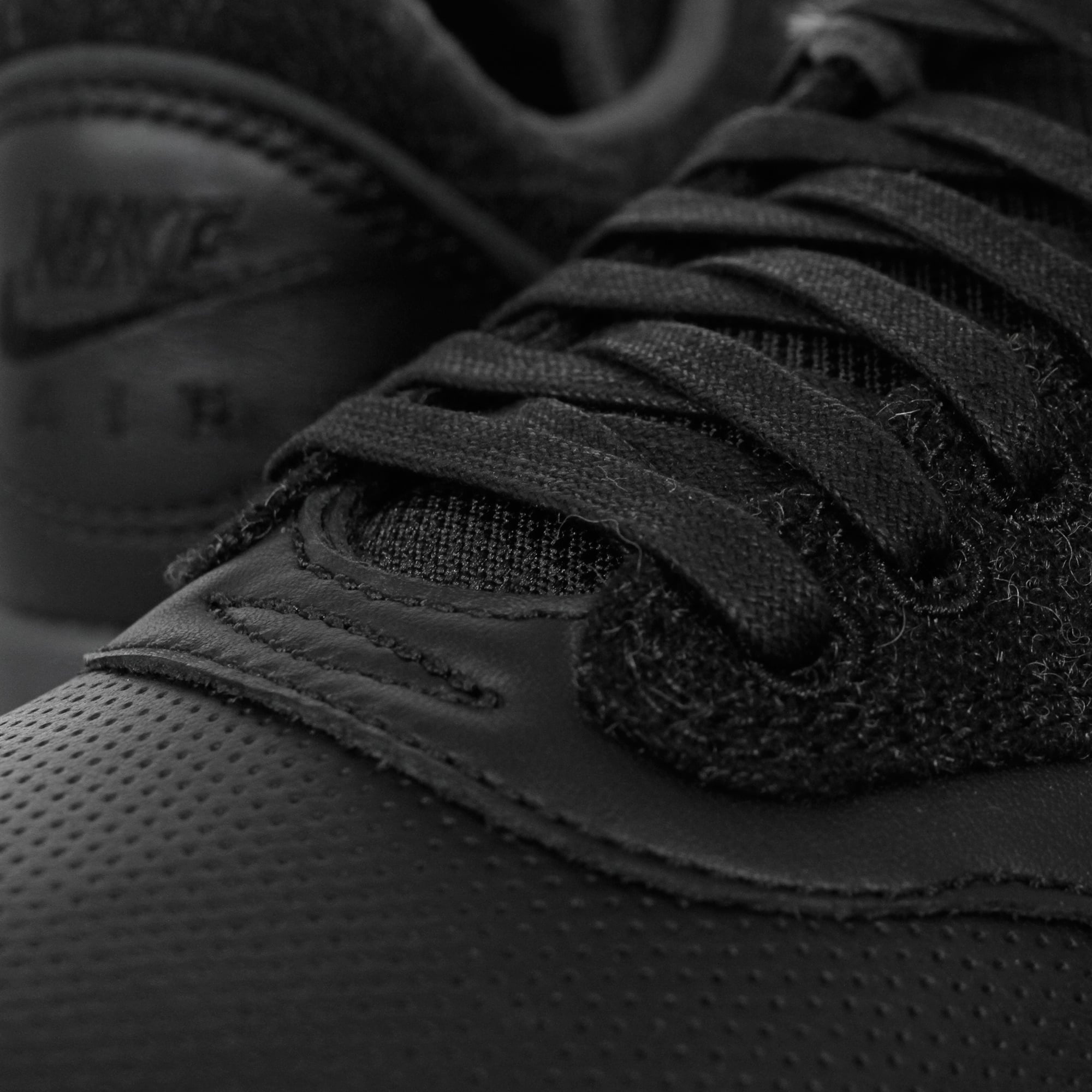 A close-up of the laces and perforated detail on a black trainer.