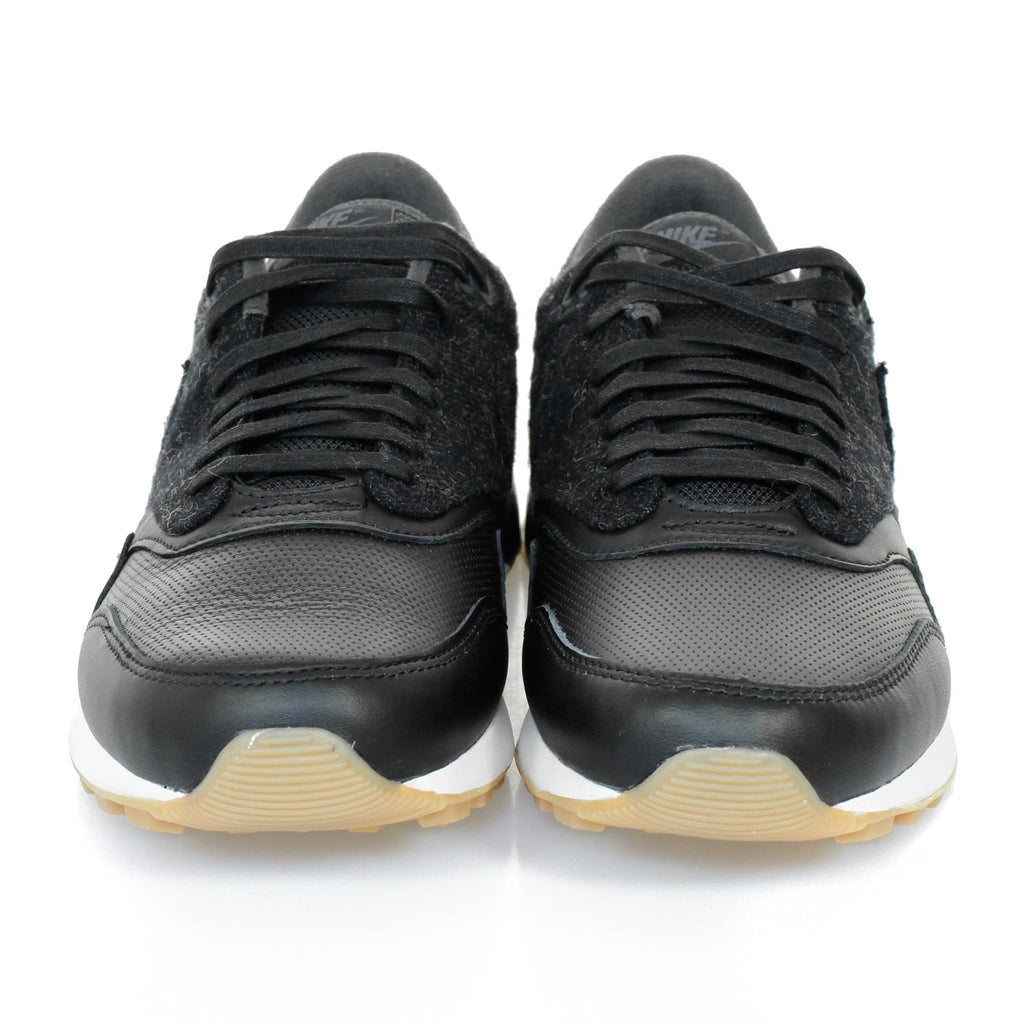 A pair of black trainers with textured uppers and white soles, viewed directly from the front.