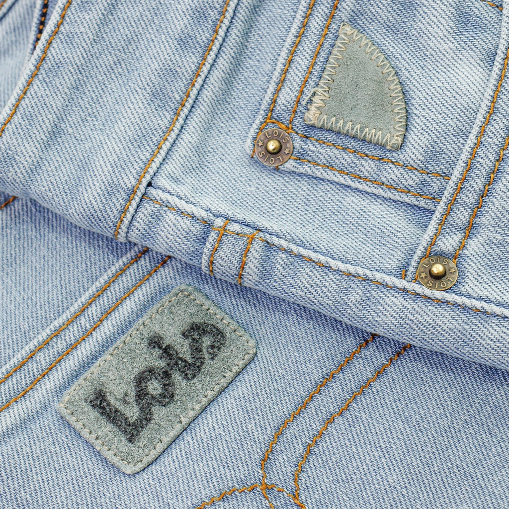 Close-up of the brand patch on light blue denim jeans with contrasting stitching.