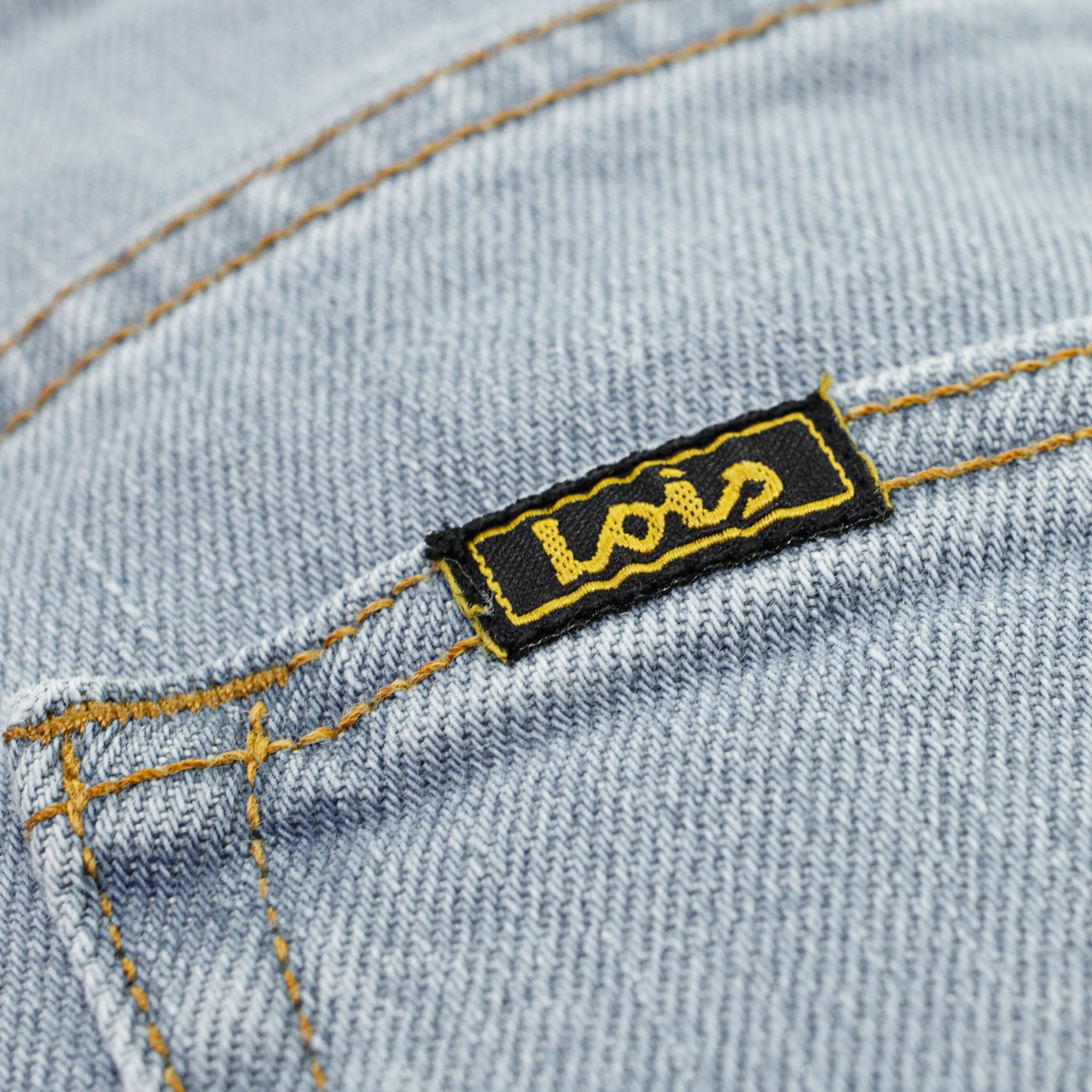 Detailed close-up of the black and yellow 'Lois' brand label on blue denim jeans.