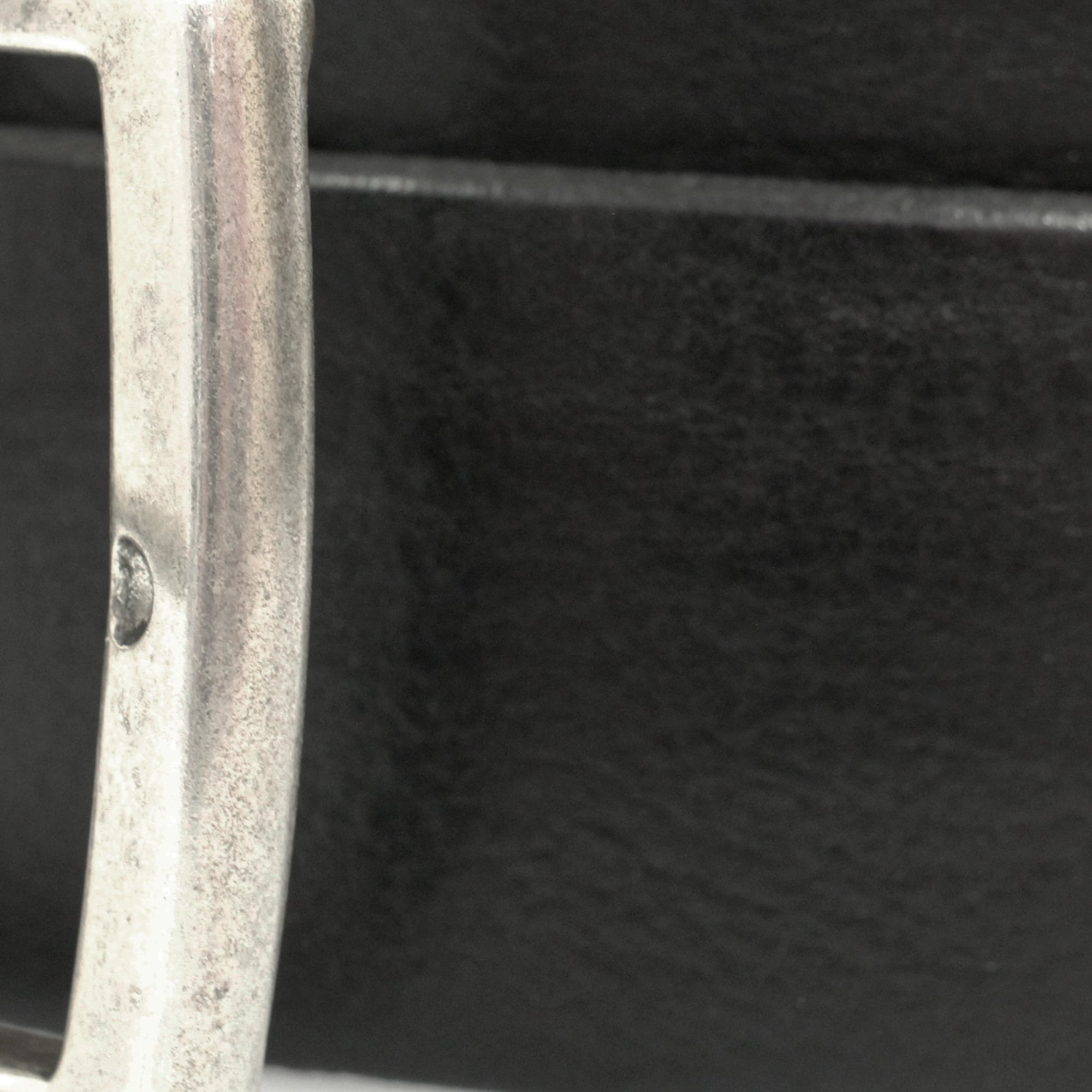 Close-up of a silver belt buckle on a black leather belt, showcasing texture and detail.