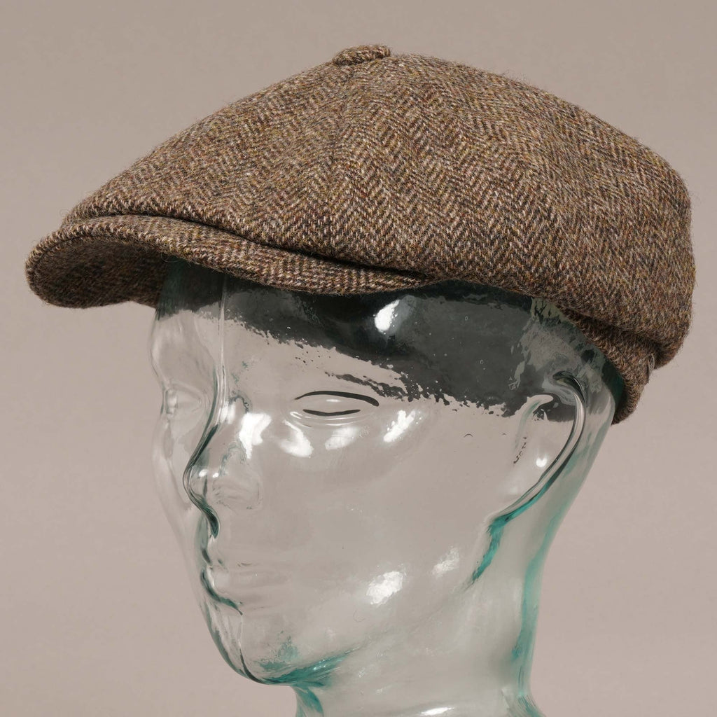 Three-quarter view of a brown herringbone flat cap on a mannequin head.