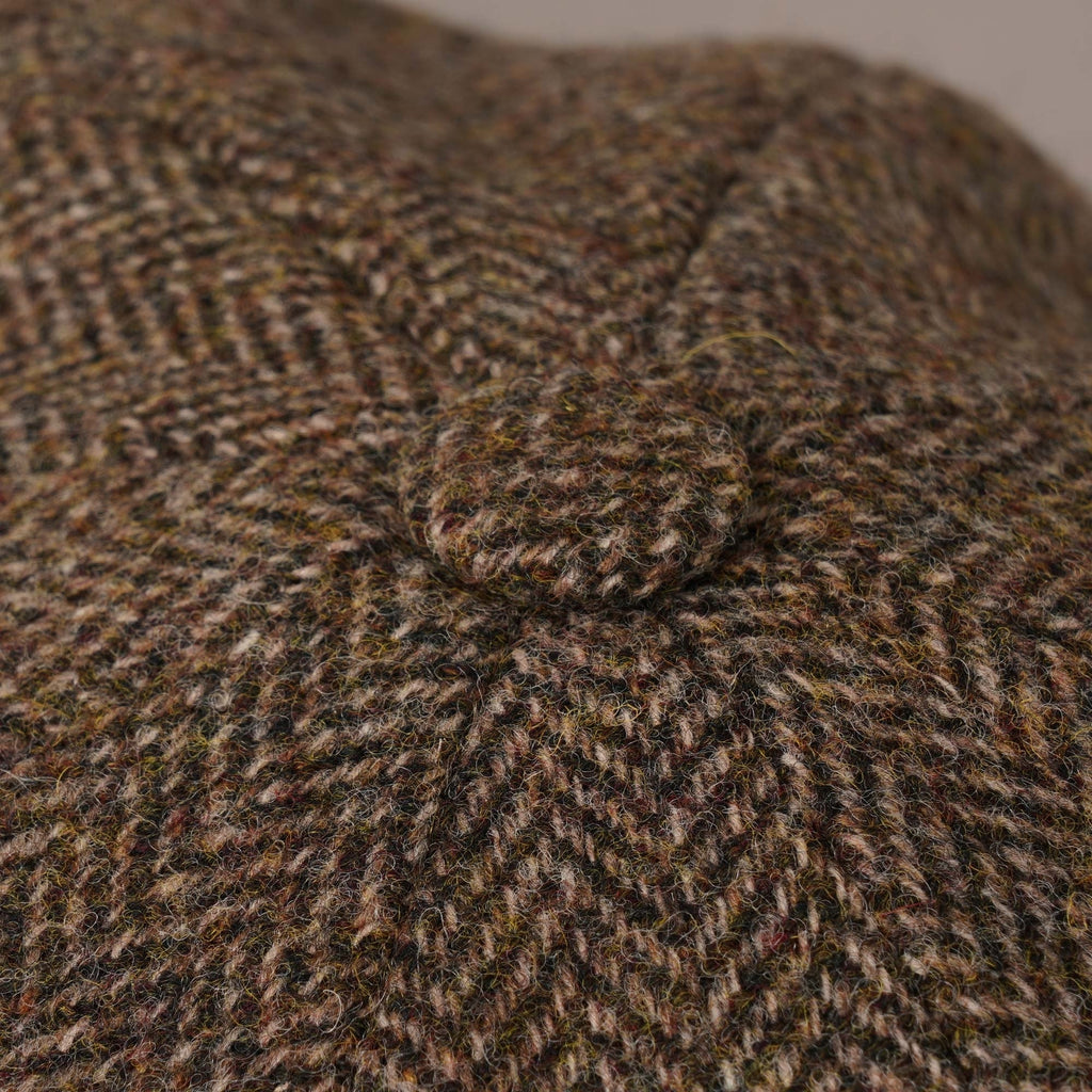Close-up of the button detail on the top of the brown herringbone flat cap.