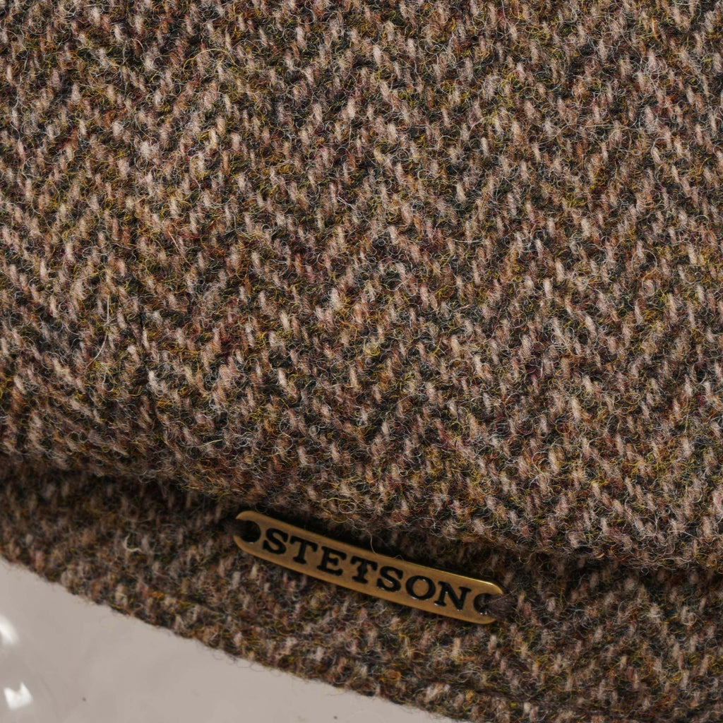 Close-up of the Stetson logo on the side of the brown herringbone flat cap.
