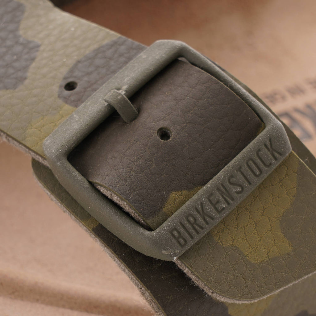 Close-up of the buckle on a green camouflage Birkenstock sandal with brand name.