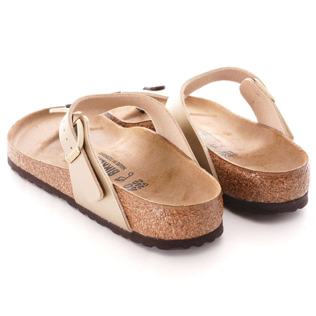 A rear view of a pair of gold-coloured Birkenstock Gizeh sandals with cork soles.