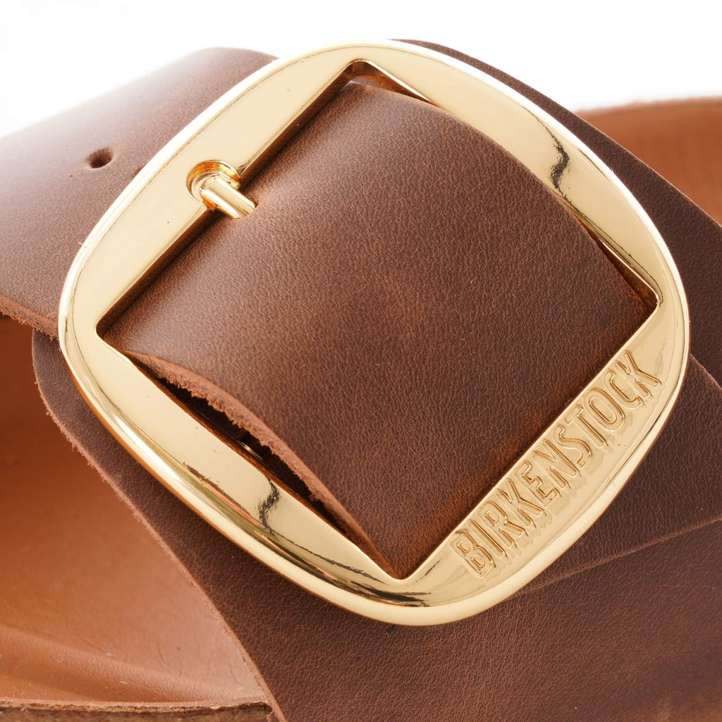 Close-up of a gold buckle on a brown sandal with 'BIRKENSTOCK' engraved.