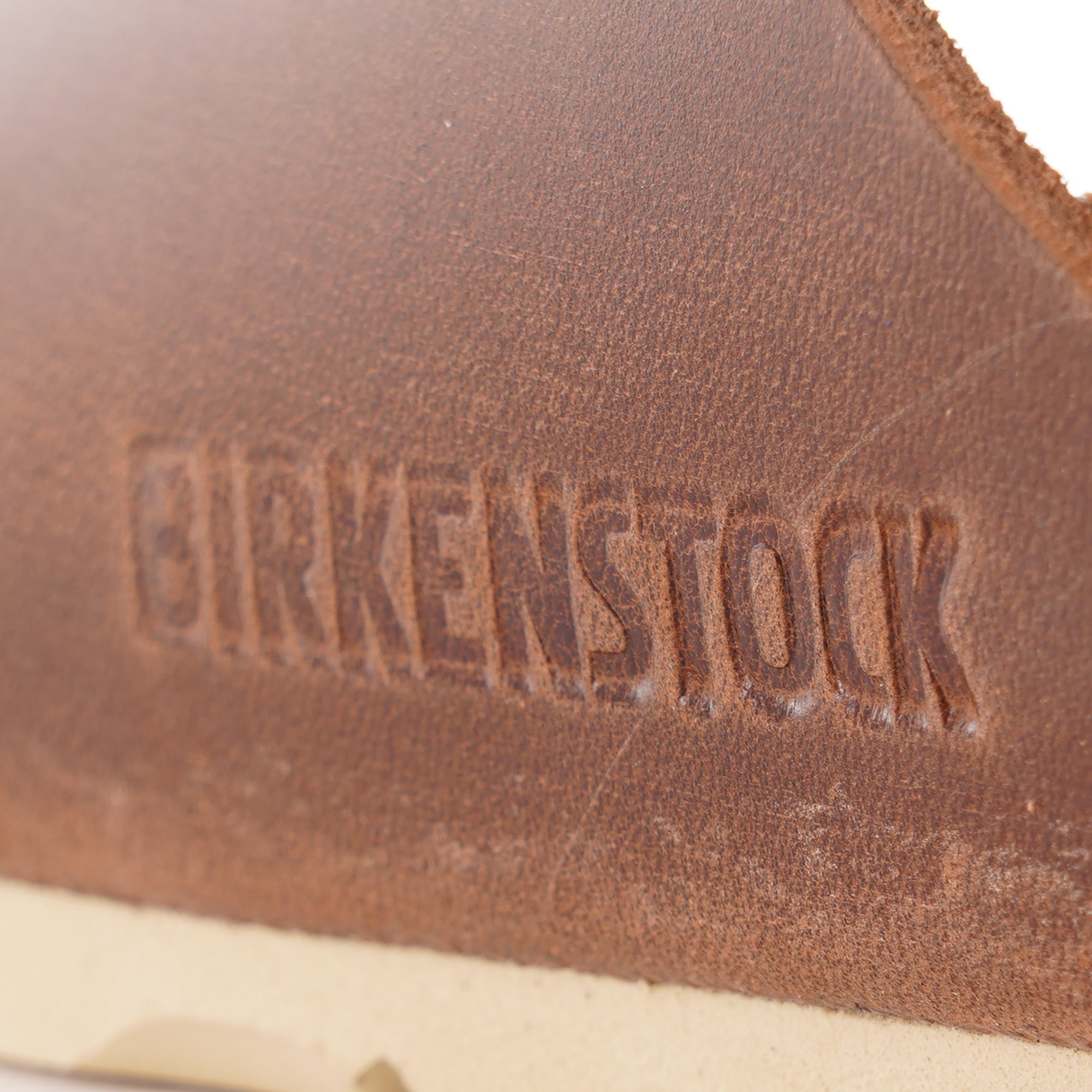 Close-up of 'BIRKENSTOCK' embossed into the brown leather of a sandal.