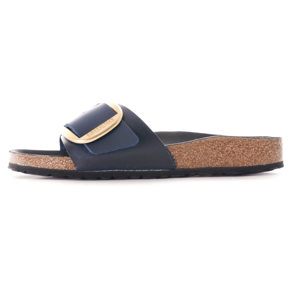 Side profile of a navy blue slip-on sandal with a large gold buckle.