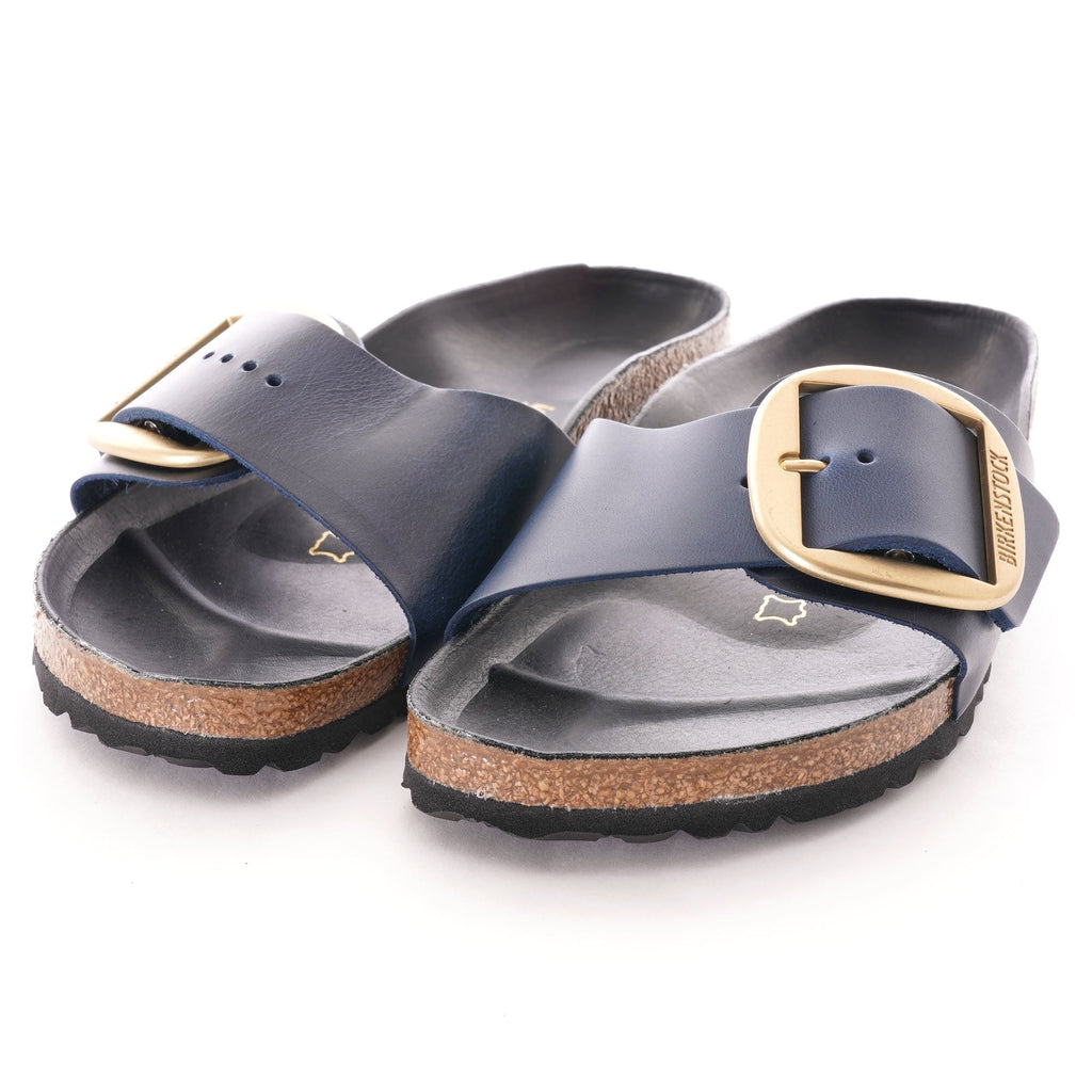 A pair of navy blue slip-on sandals with large gold buckles.