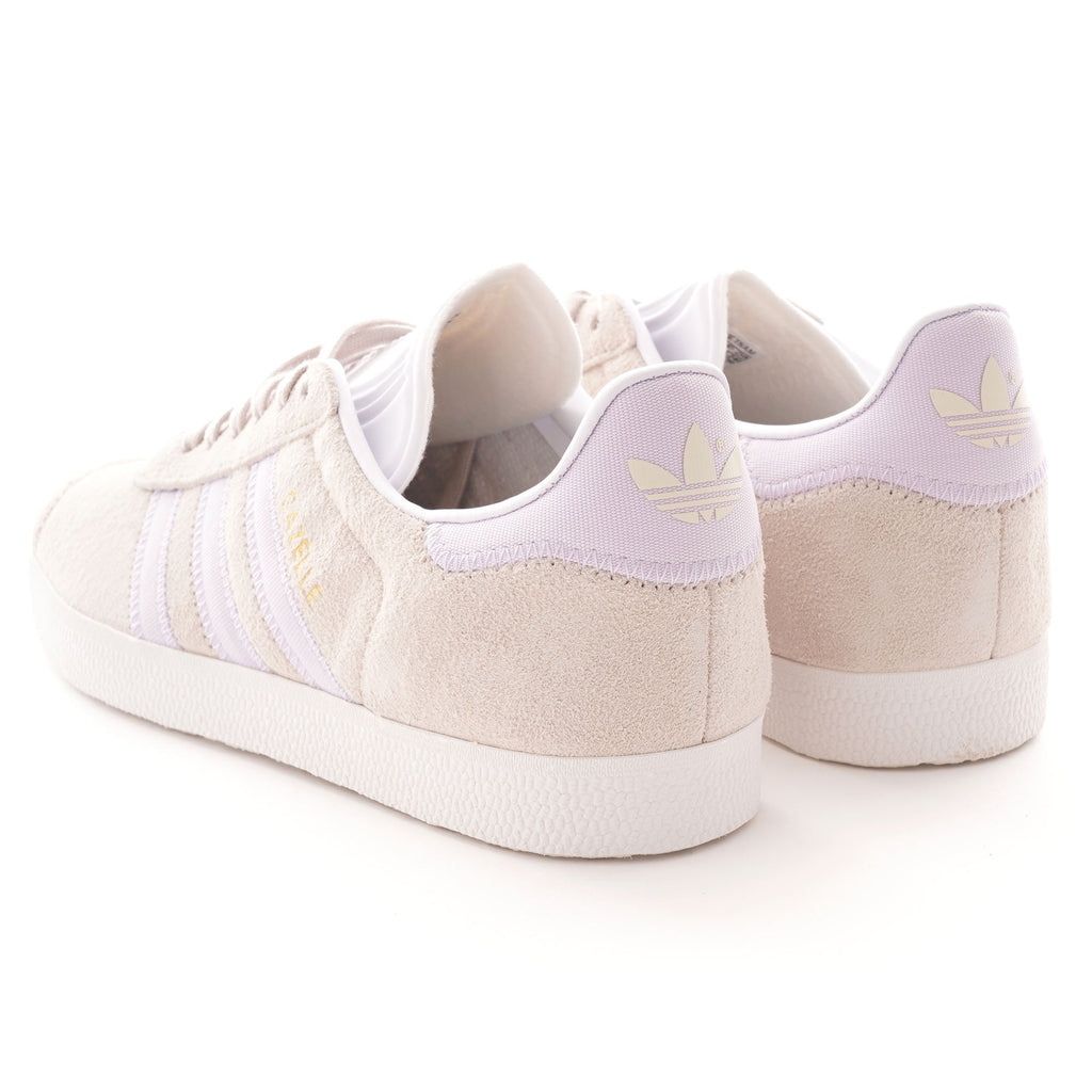 Rear view of two pale beige Adidas Gazelle trainers with purple heel tabs.