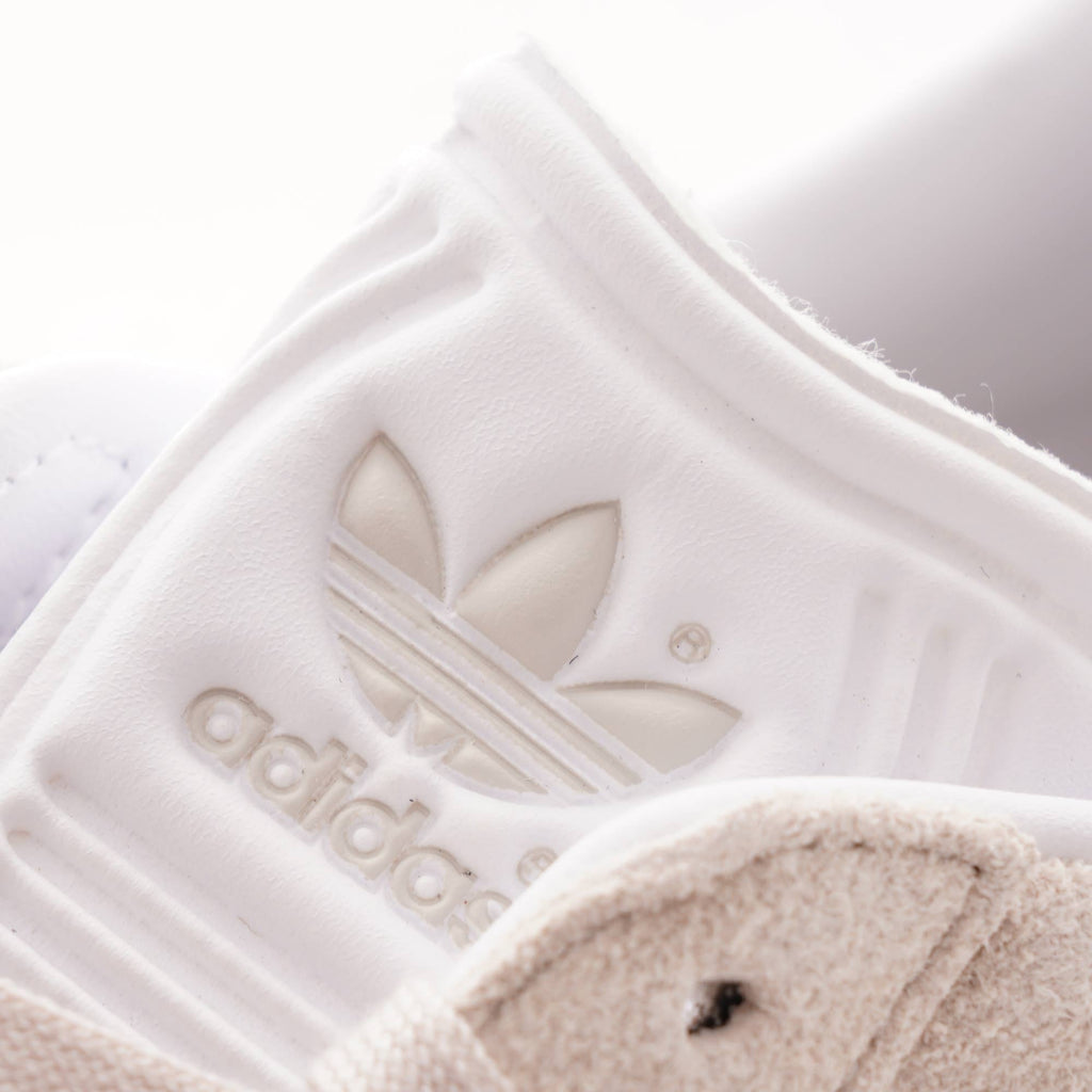 Close-up of the Adidas logo on the tongue of a pale beige trainer.
