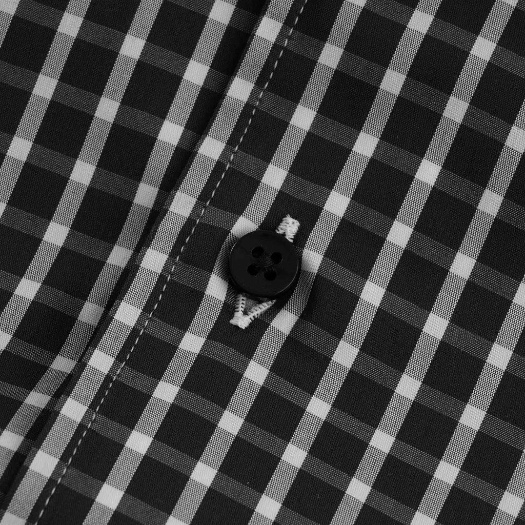 A close-up of a black button and stitching on the checked shirt.
