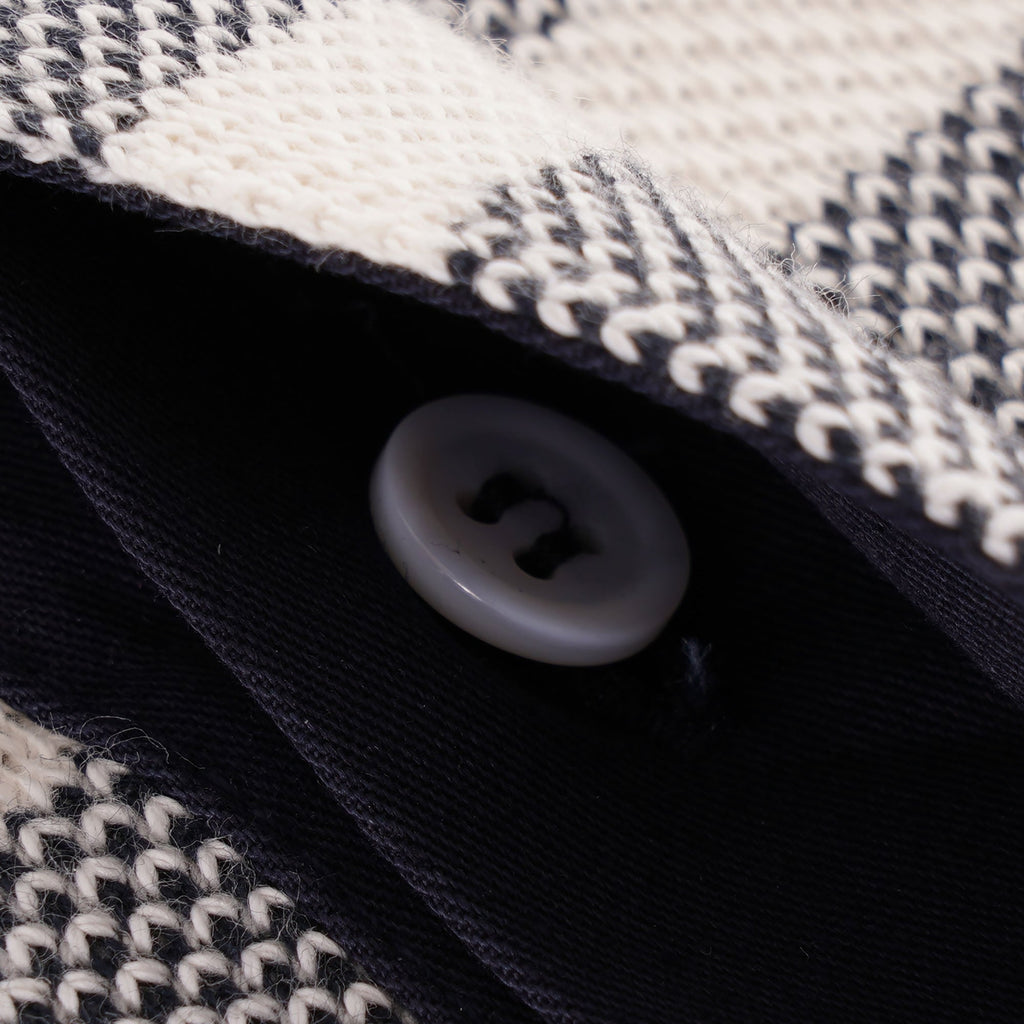 Detailed view of a single grey button on the placket of the striped long-sleeved polo shirt.