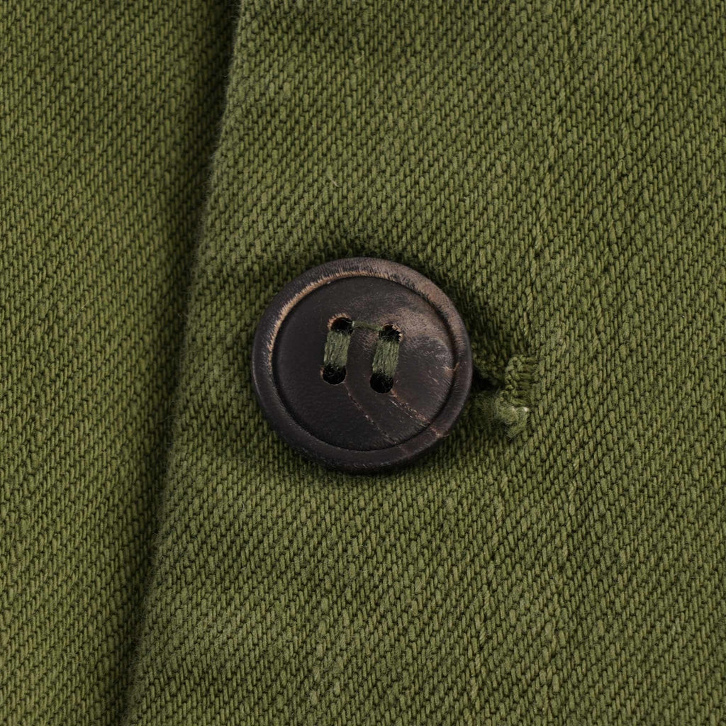 Close-up of a dark, textured button on an olive green fabric.