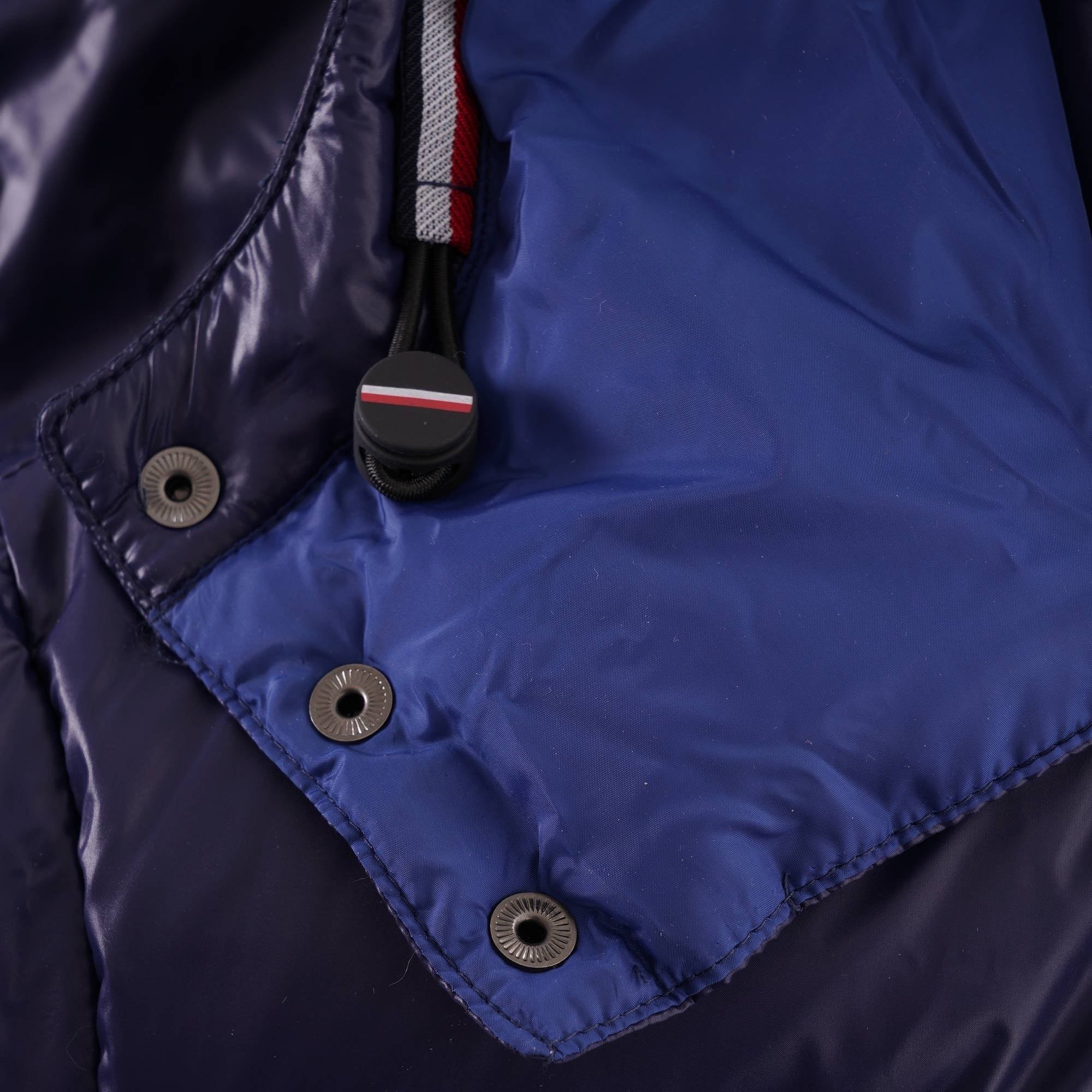 A close-up of the hood area with snap buttons and a drawstring, on the navy blue puffer jacket.