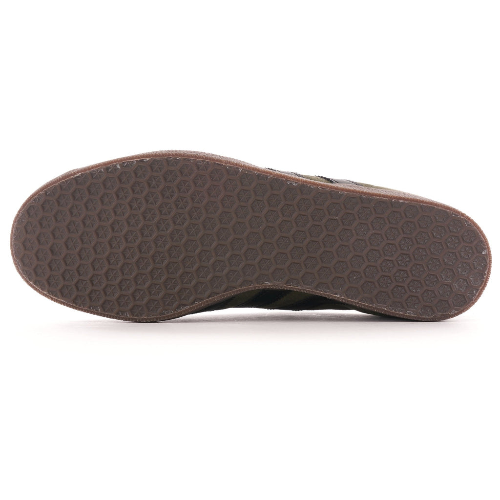 The brown hexagonal textured sole of an olive green Adidas Gazelle trainer. 
