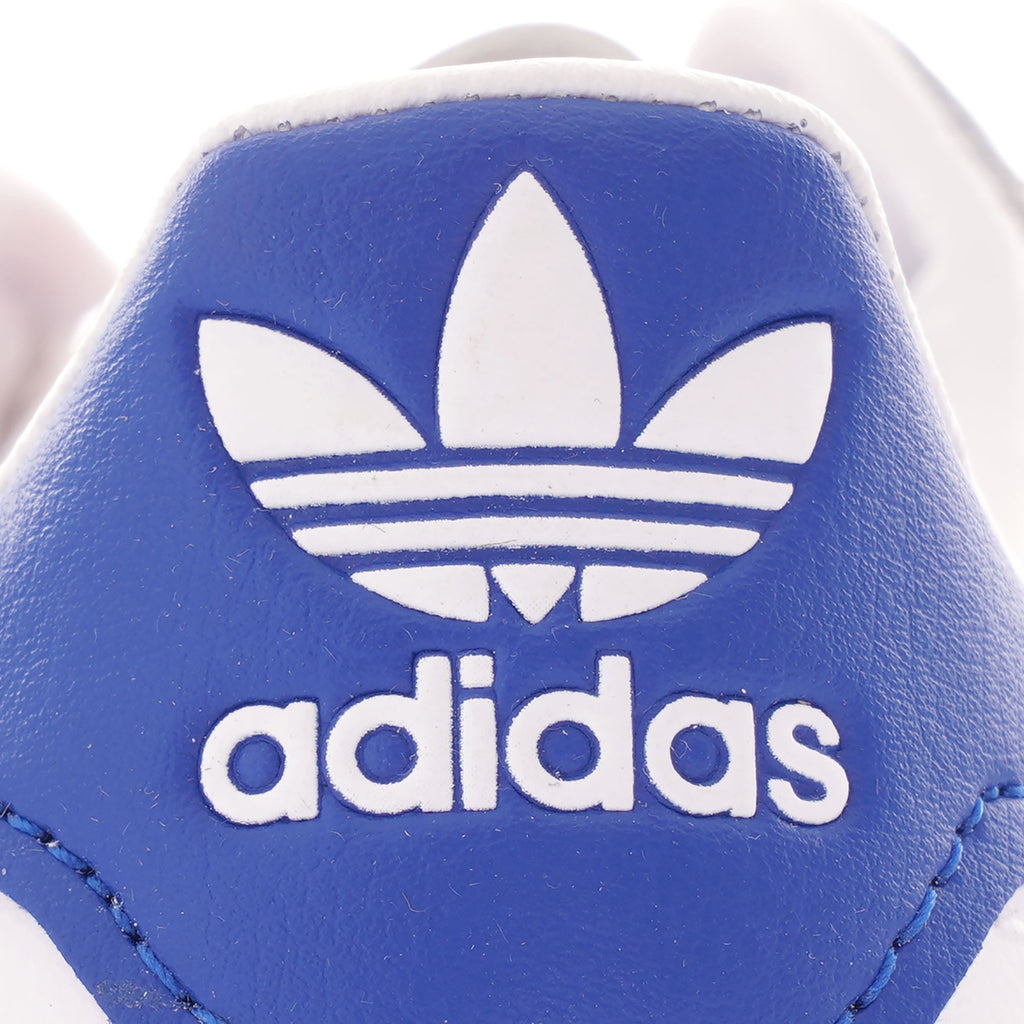 A close-up of the blue Adidas logo on the heel of a white Adidas trainer.