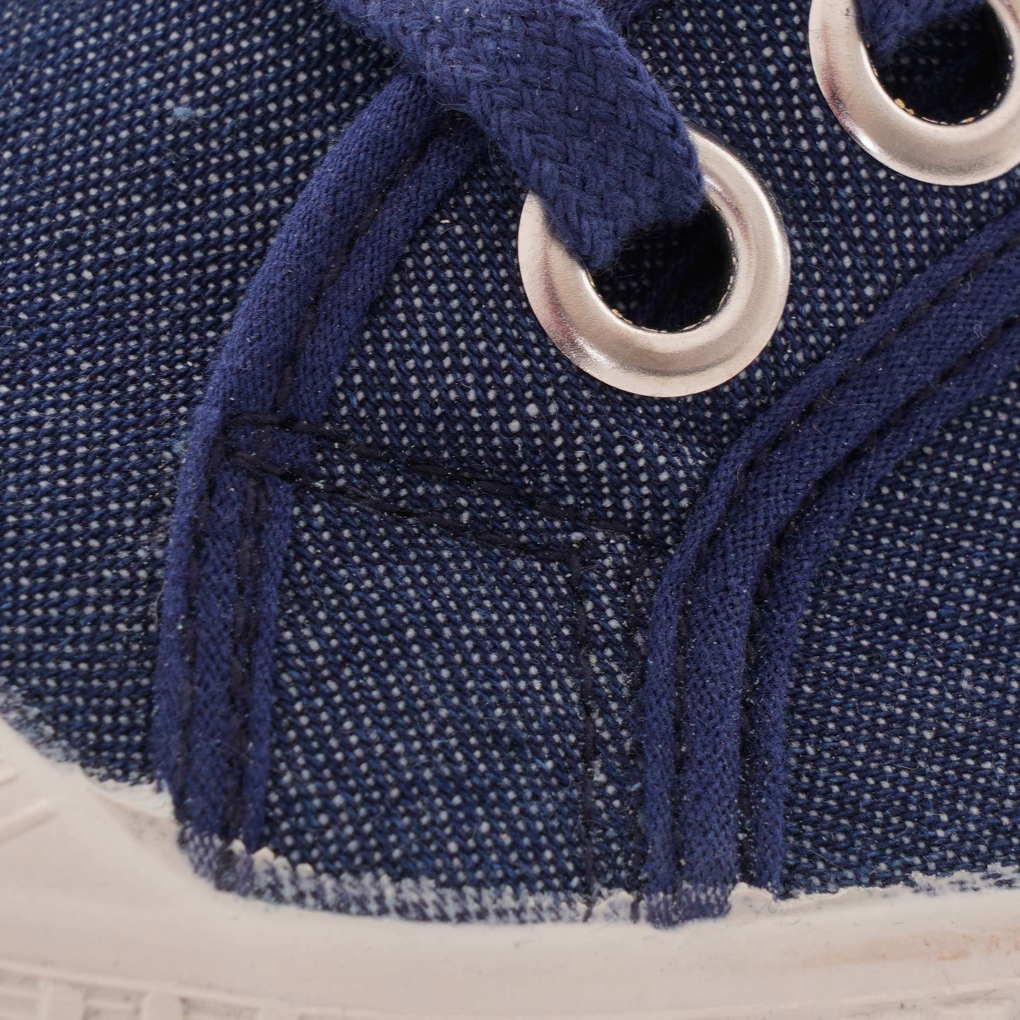 Close-up of the navy blue canvas fabric and white eyelets with laces on the shoe.