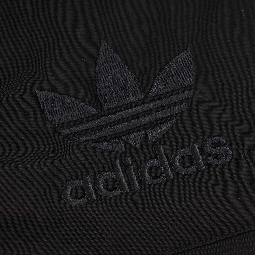 A close-up of the black embroidered Adidas logo on the black jacket.