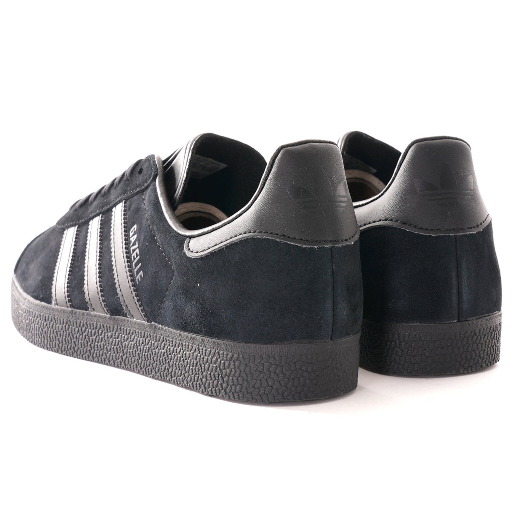 A pair of black Adidas Gazelle trainers, photographed from an angled rear view.