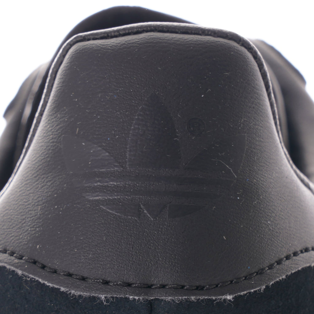 A close-up of the Adidas Trefoil logo embossed on the heel of a black trainer.