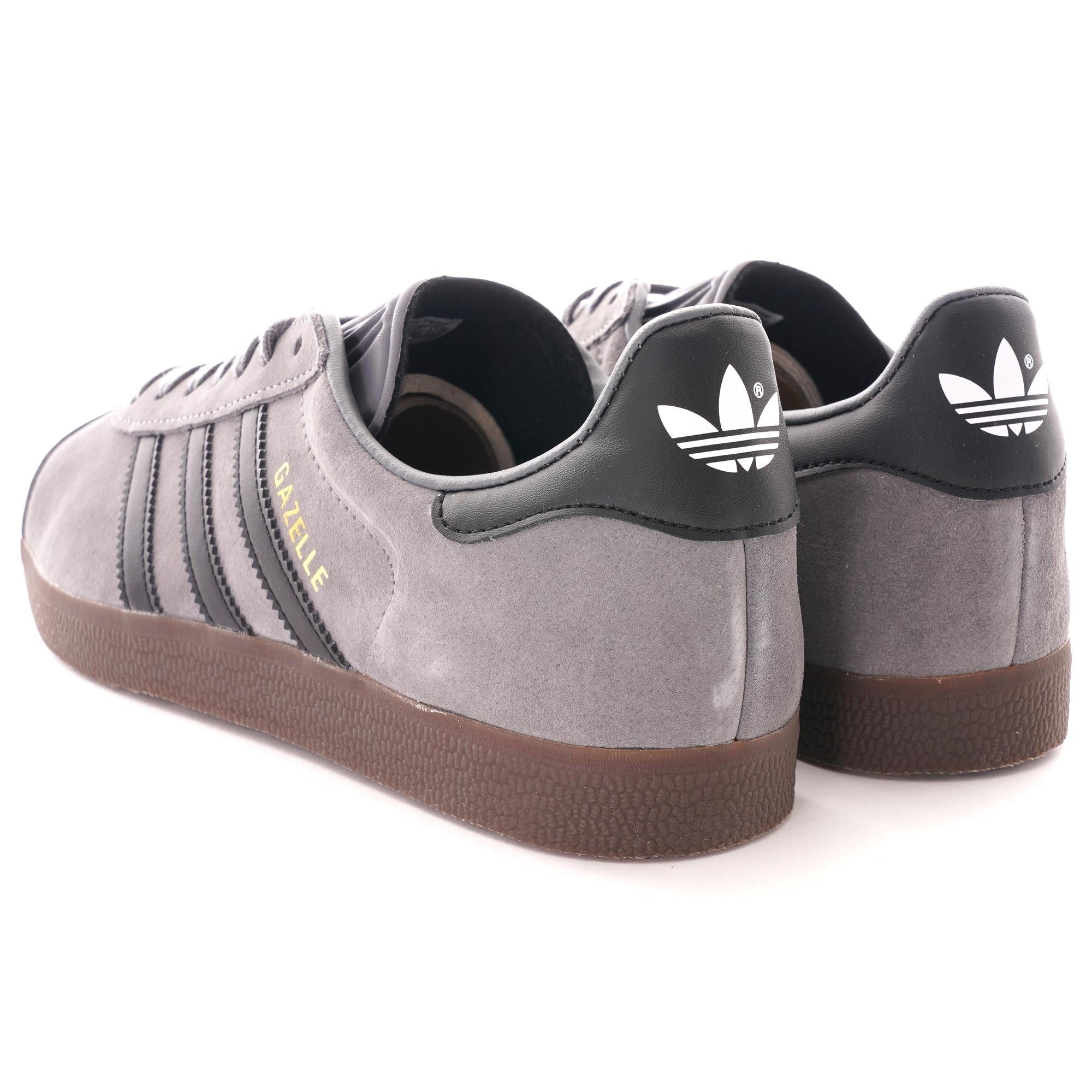 The rear view of two grey Adidas Gazelle trainers, showing the black heel tabs with white logos.