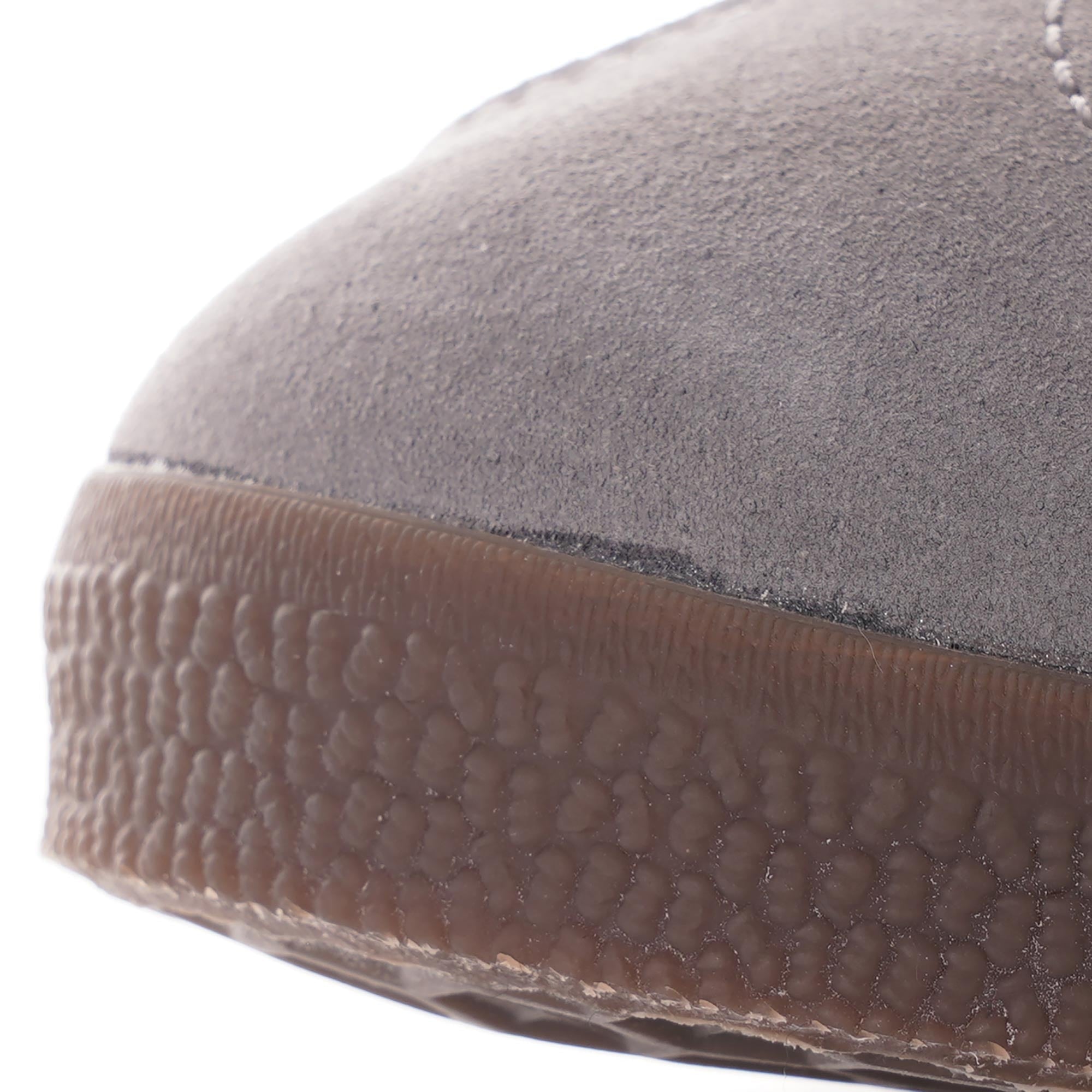 A close-up of the textured brown sole and grey suede toe of an Adidas Gazelle trainer.