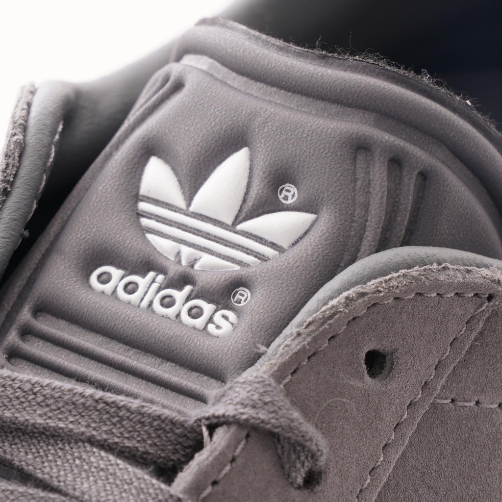 A close-up of the grey tongue of an Adidas Gazelle trainer, showing the white Adidas logo.
