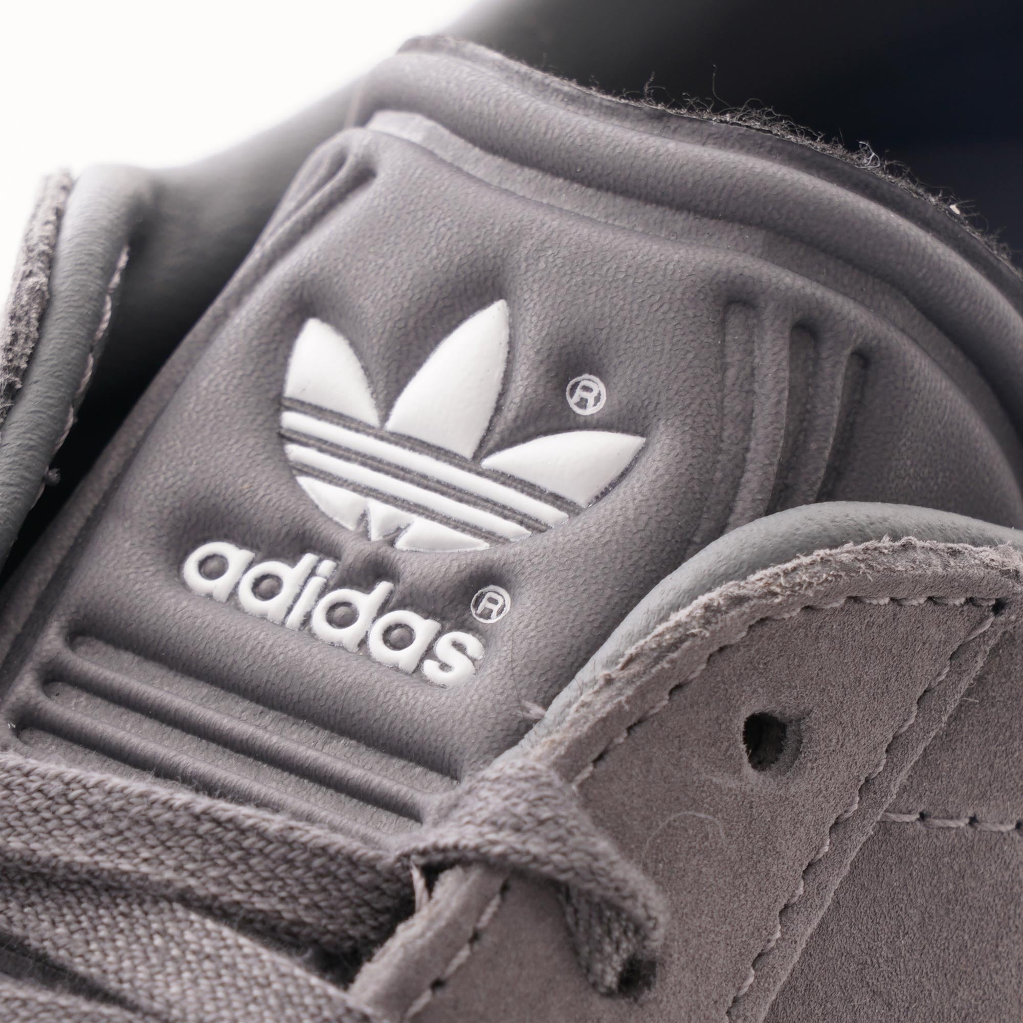 A close-up of the grey tongue of an Adidas Gazelle trainer, showing the white Adidas logo.