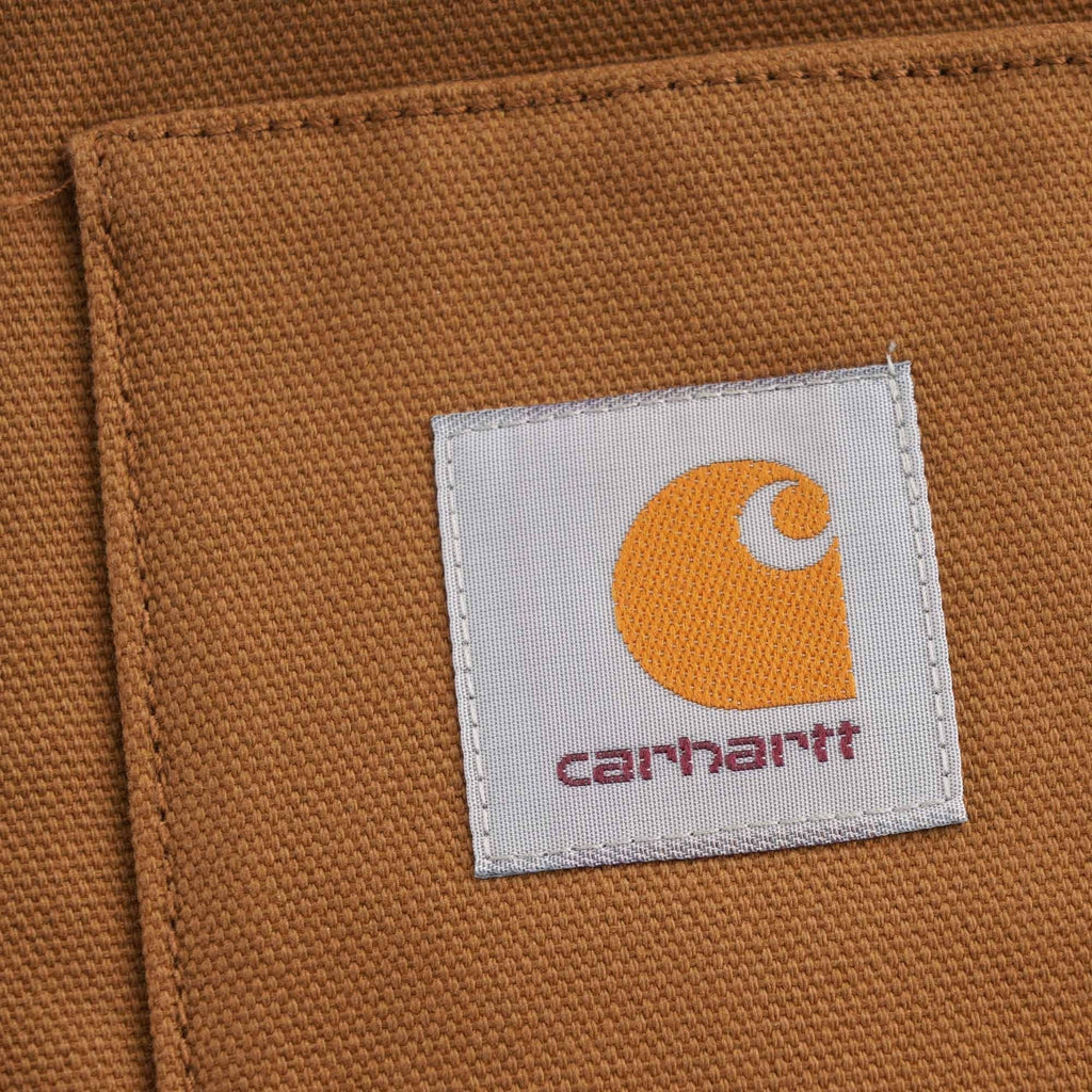 Close-up of the iconic Carhartt 'C' logo patch on the front pocket of the brown vest.