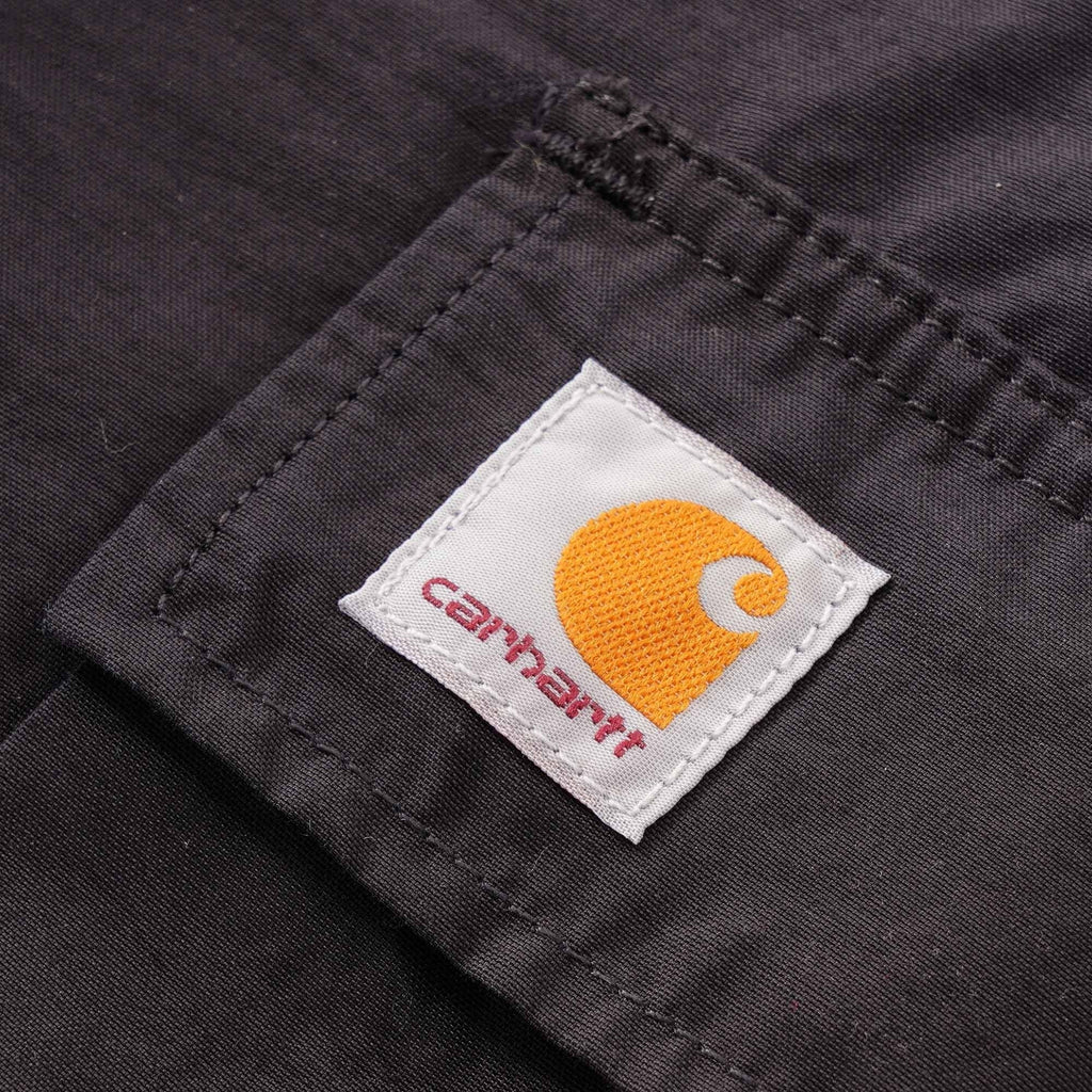 A close-up of the Carhartt WIP logo patch on the dark grey cargo trousers.