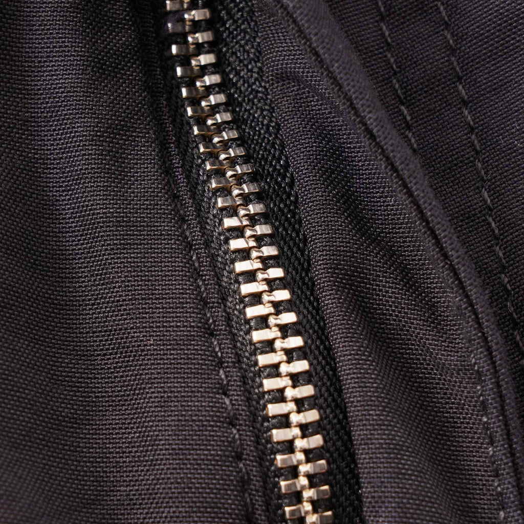 A close-up of the silver zipper on the dark grey cargo trousers.