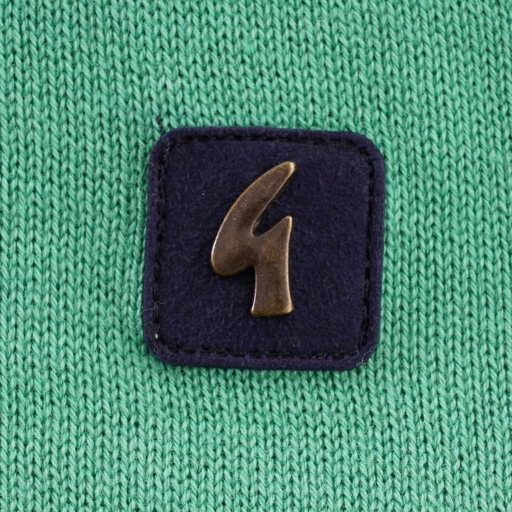 A close-up of the brand logo on the green knitted polo shirt.