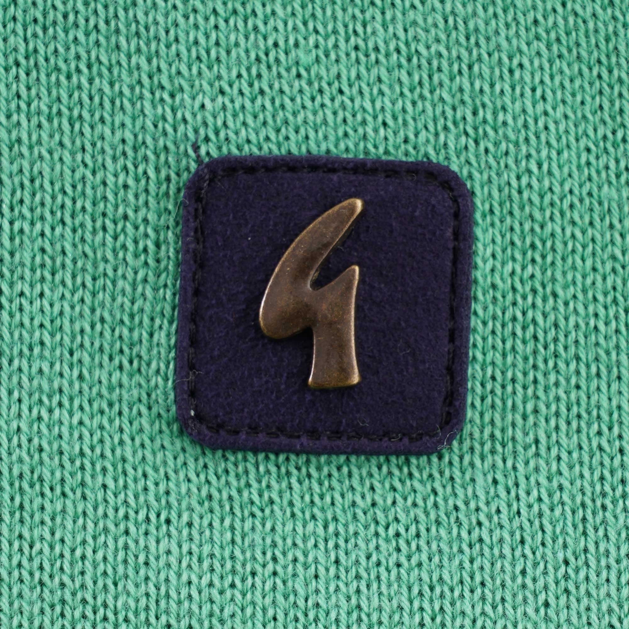 A close-up of the brand logo on the green knitted polo shirt.