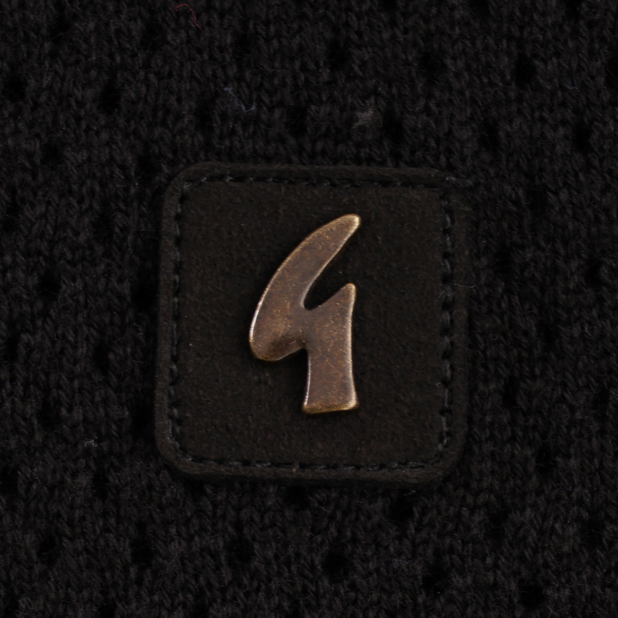Close-up of the Gabicci logo on a small leather patch on a black knitted top.