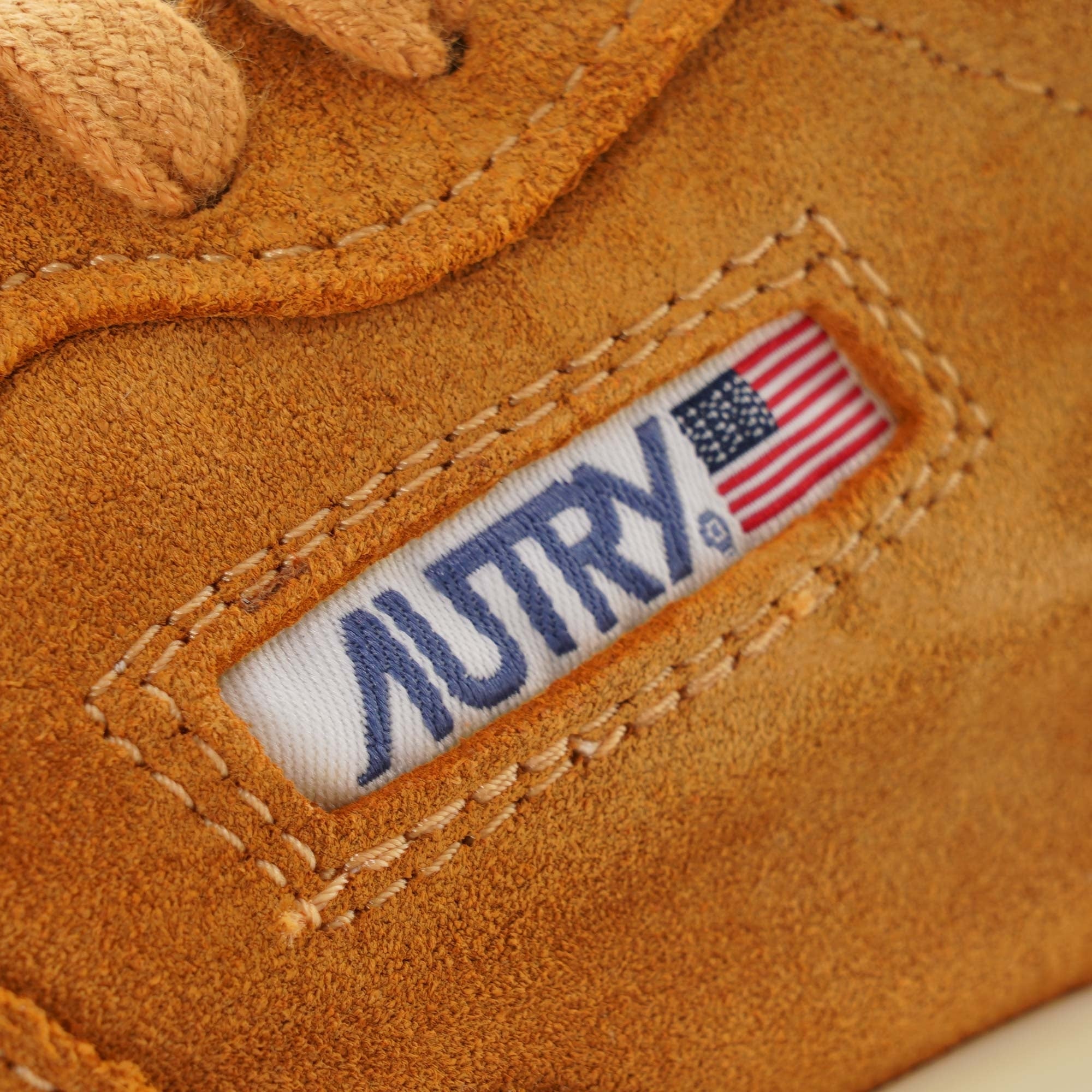 Close-up of the Autry logo tag with the American flag on a tan suede trainer.
