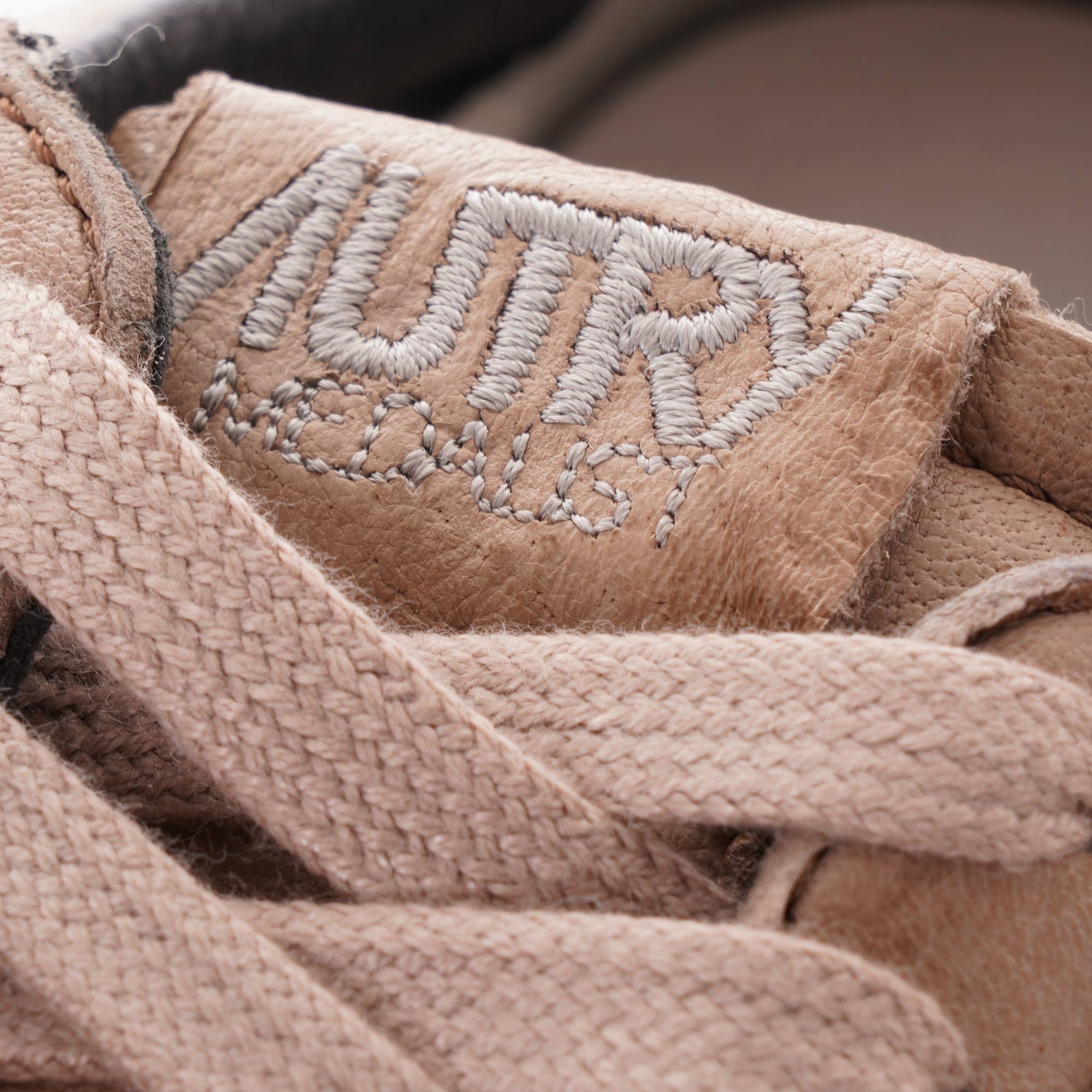 Close-up of the Autry logo embroidered on the tongue of a grey-brown leather sneaker.