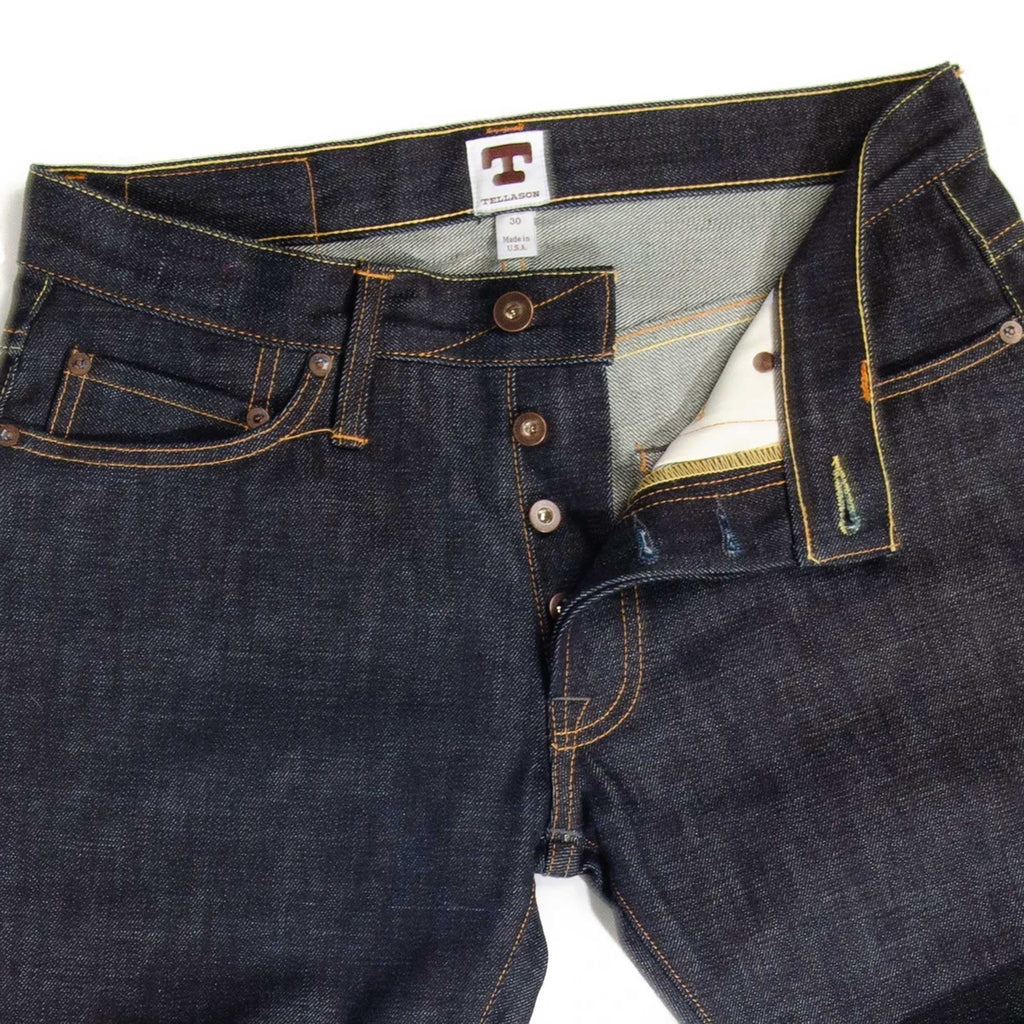 Close-up of the fly and waist of dark blue denim jeans with button details.