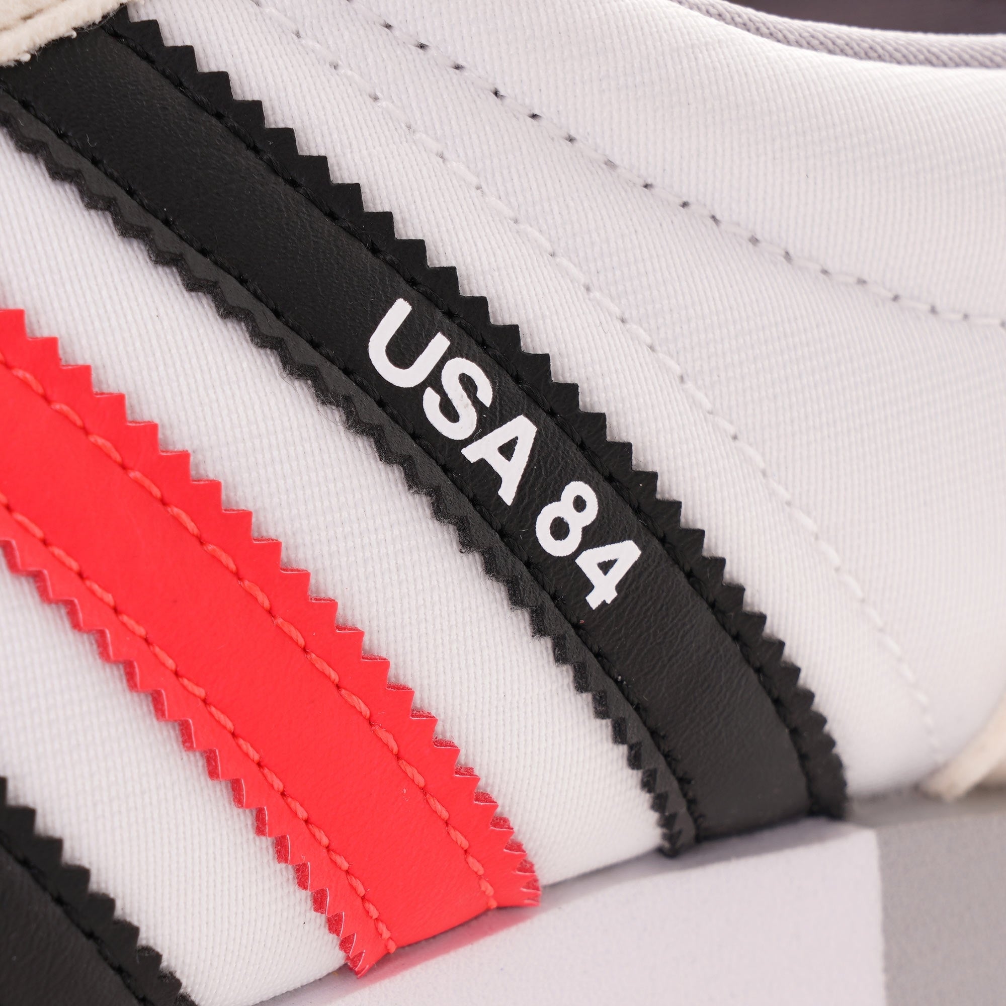 A close-up of the red and black stripes on an Adidas USA 84 trainer.