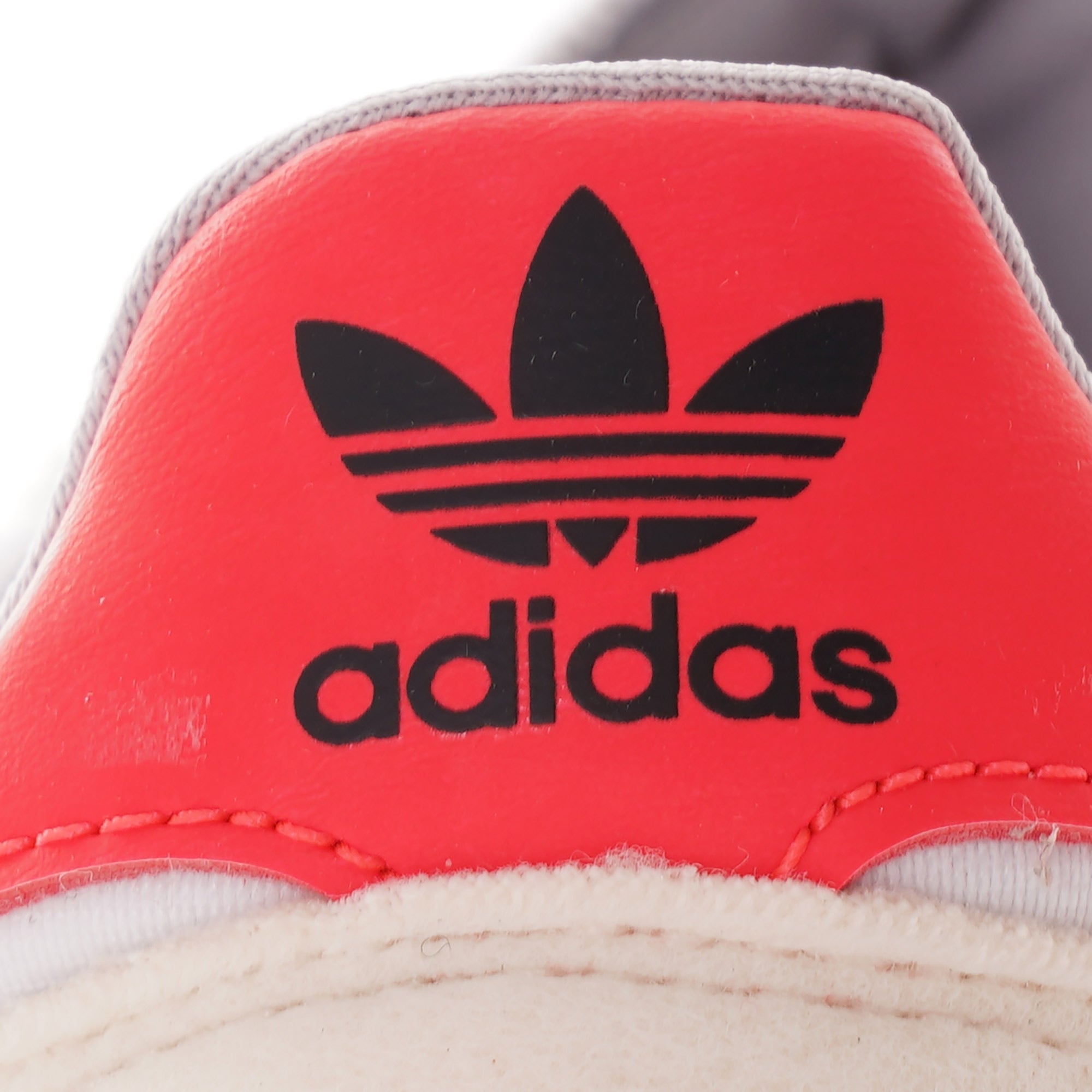 A close-up of the red heel with the black Adidas logo.
