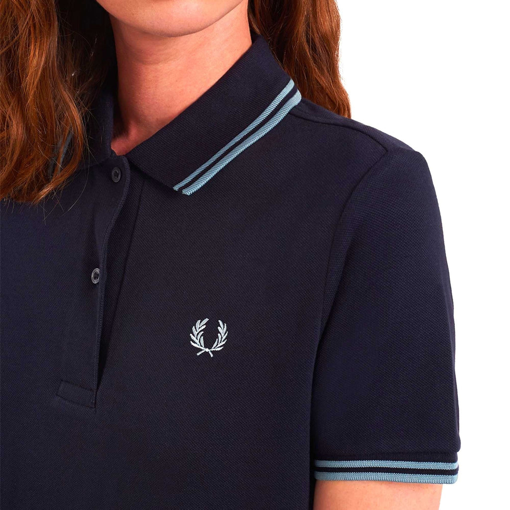 A close-up of a navy polo shirt dress, showing the collar, buttons, logo, and sleeve trim.