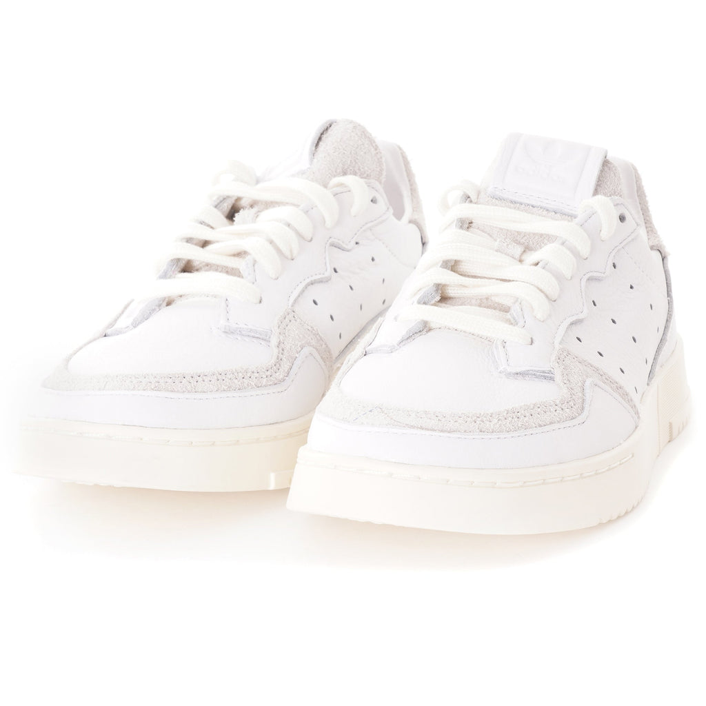 A pair of white adidas Supercourt sneakers, showing the front with laces.