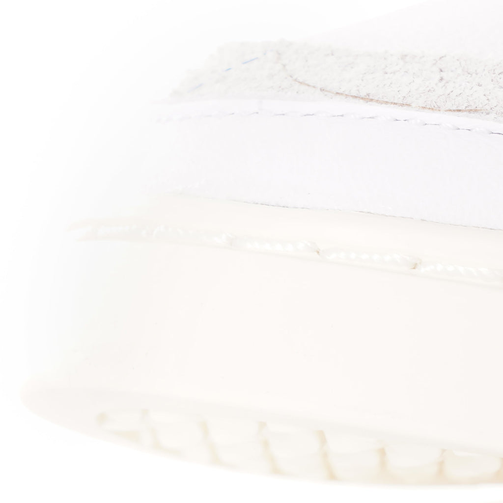 A close-up of the textured cream sole and white upper of an adidas Supercourt sneaker.