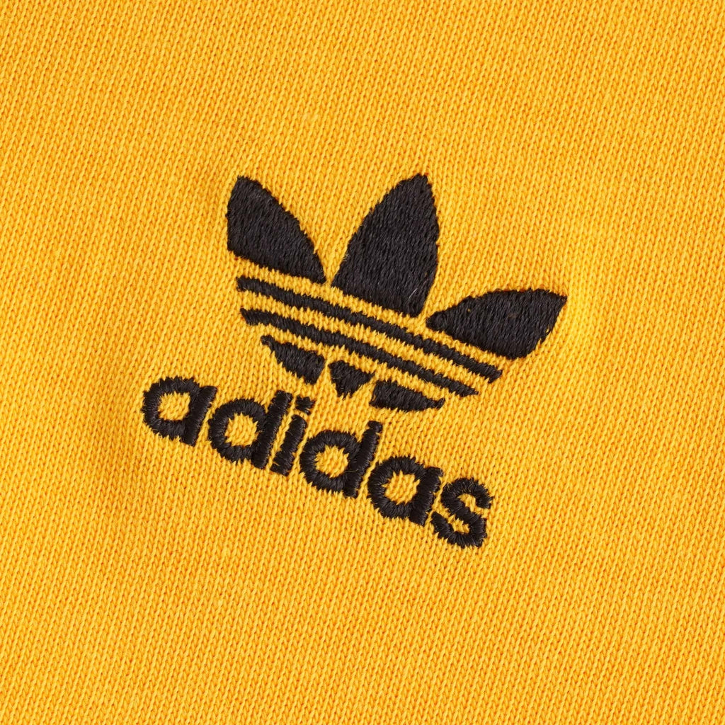 A close up of the black embroidered adidas trefoil logo on the orange t-shirt.